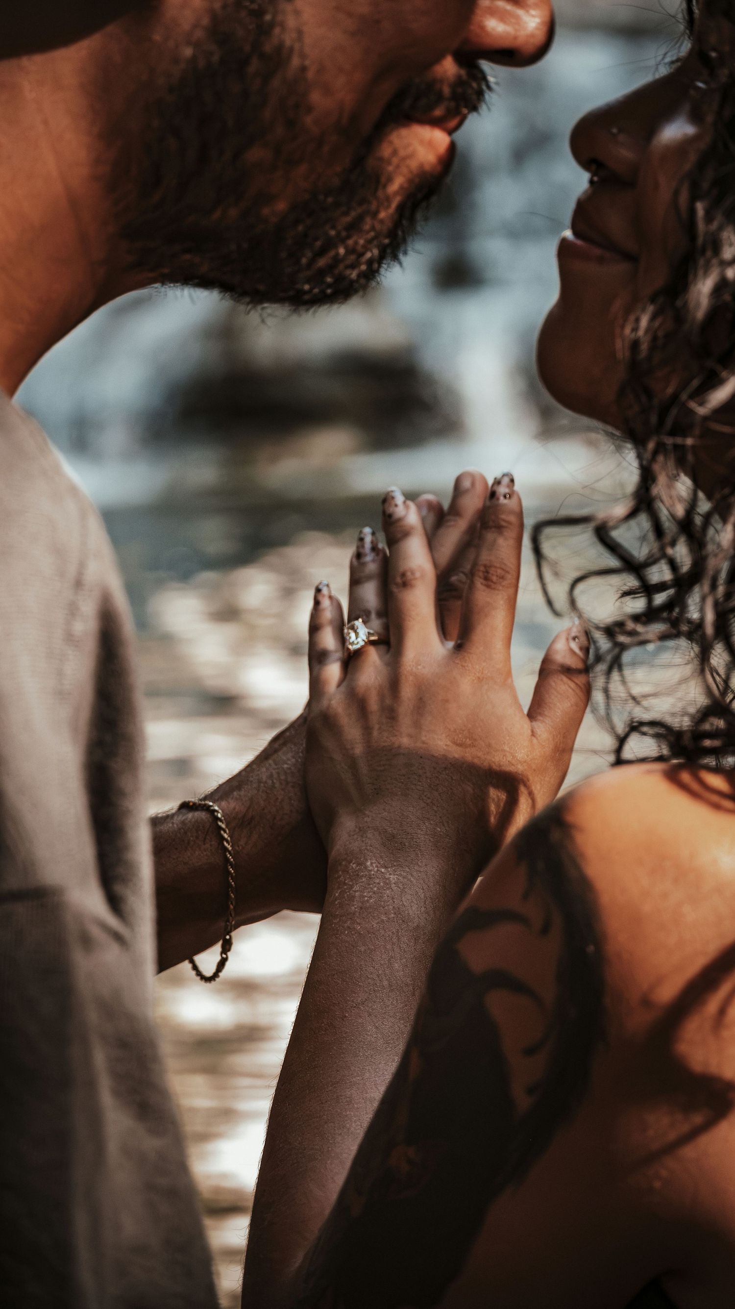 Close-up of engaged couple holding hands near water, showcasing a beautiful diamond engagement ring on womans finger.