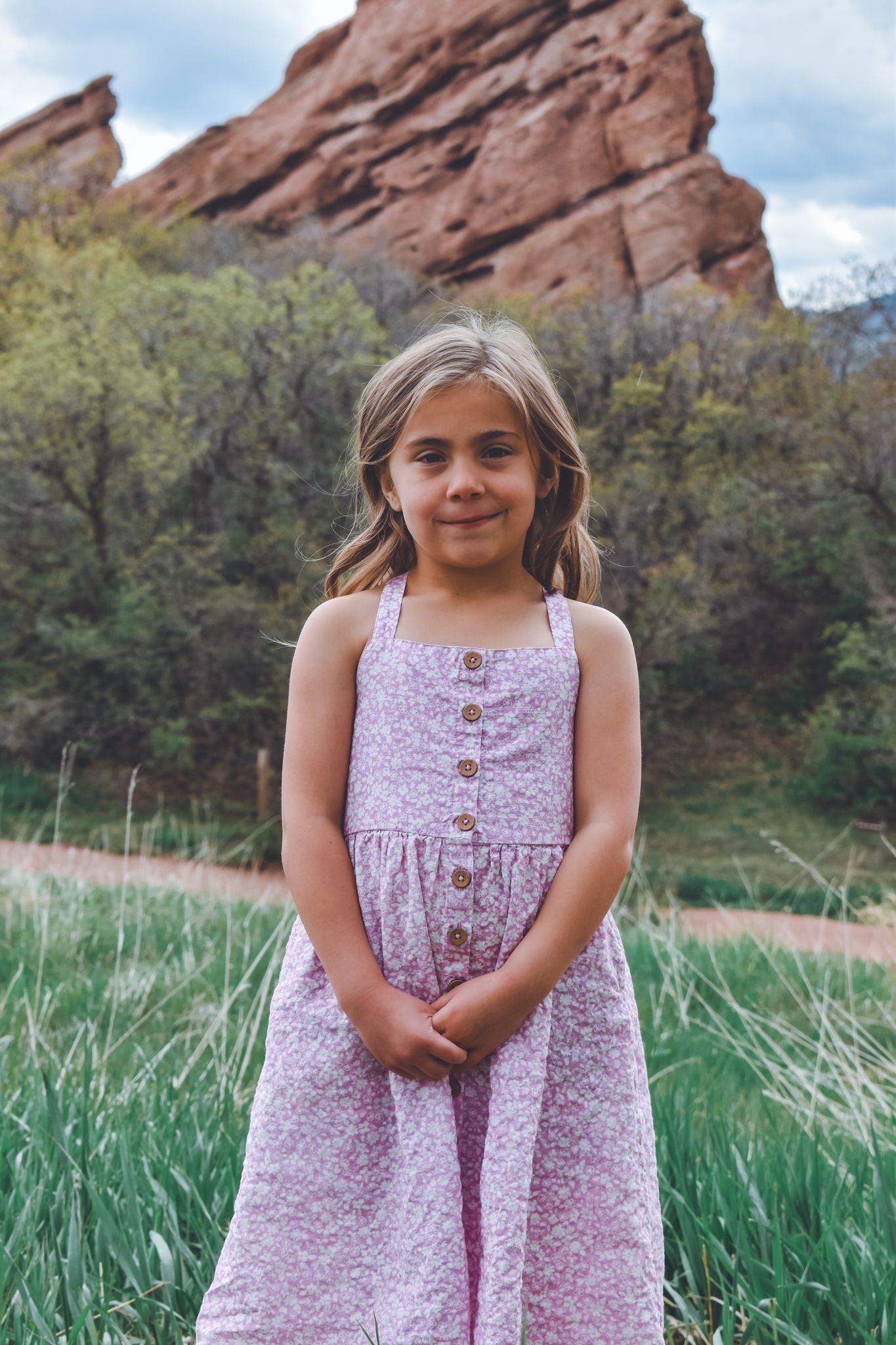 Young girl in purple floral sundress standing before red rock formations in Colorado.