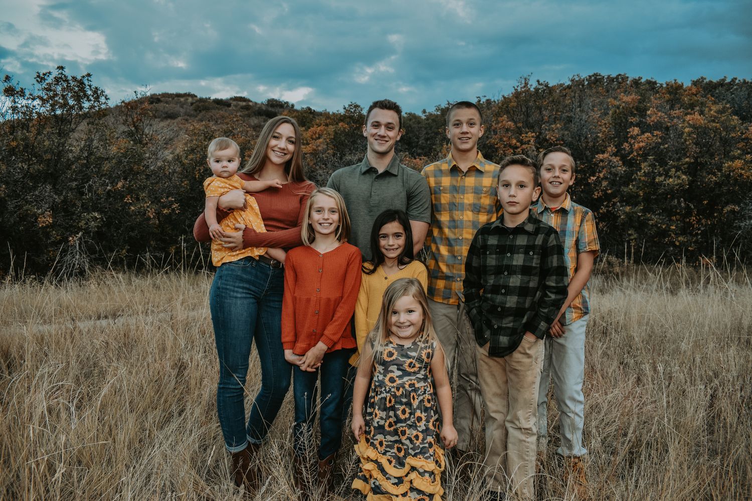 Eight children posing for a family portrait in a golden autumn field with fall foliage background.