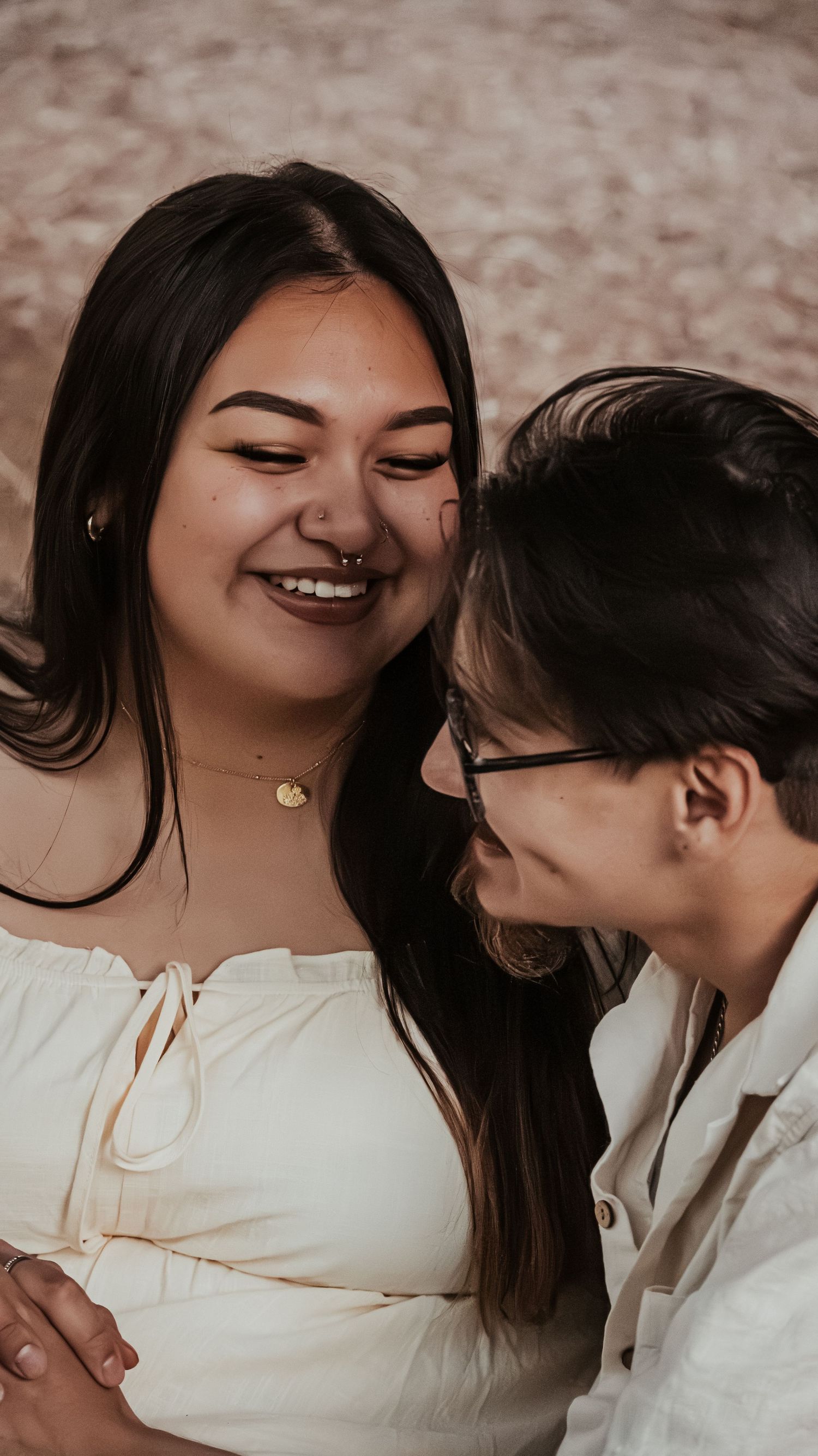 A smiling woman with a nose ring leans close to her partner during a romantic photo session.