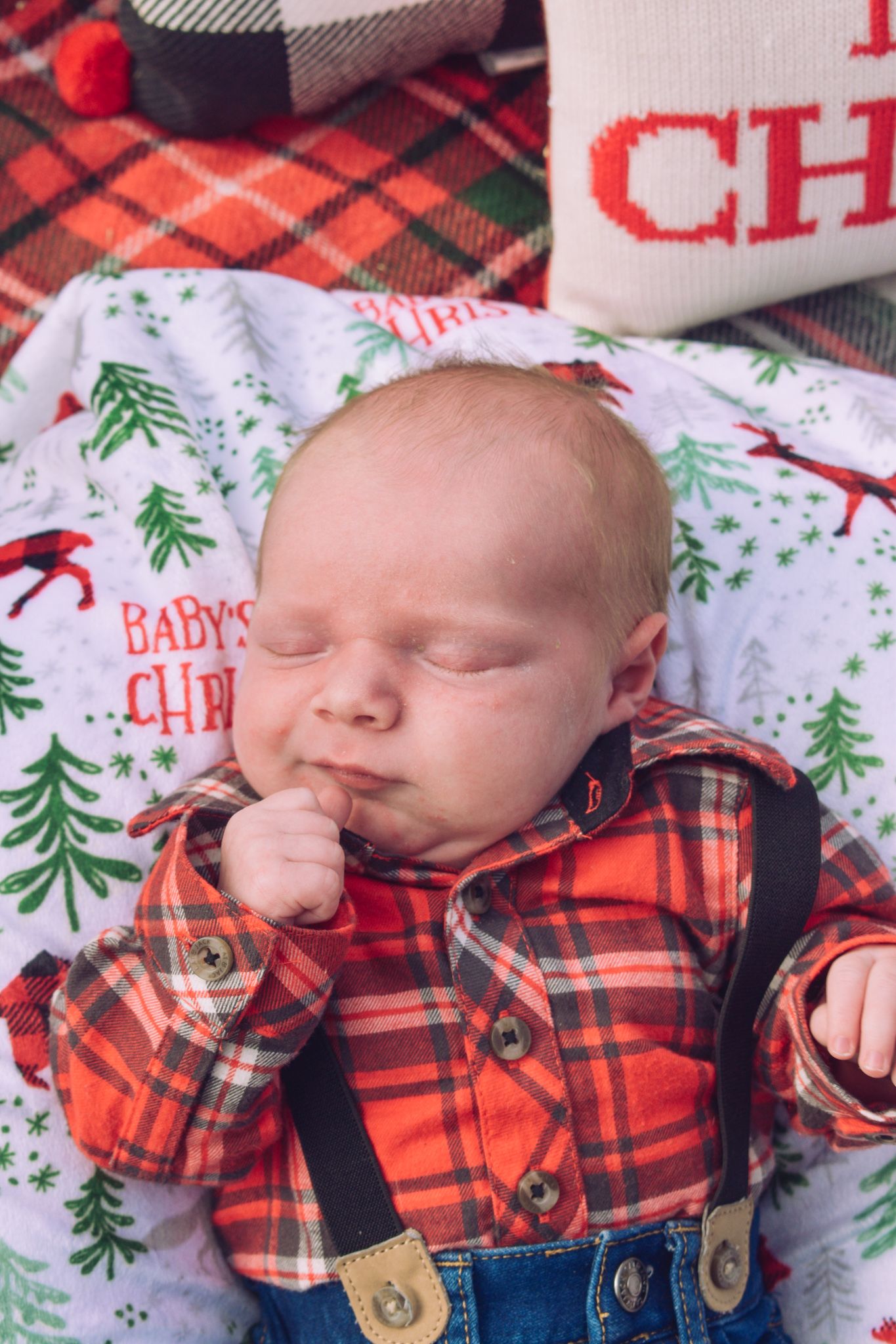 Sleeping newborn baby in red plaid shirt and suspenders on Christmas blanket. Family Photographer in Pflugerville, Tx