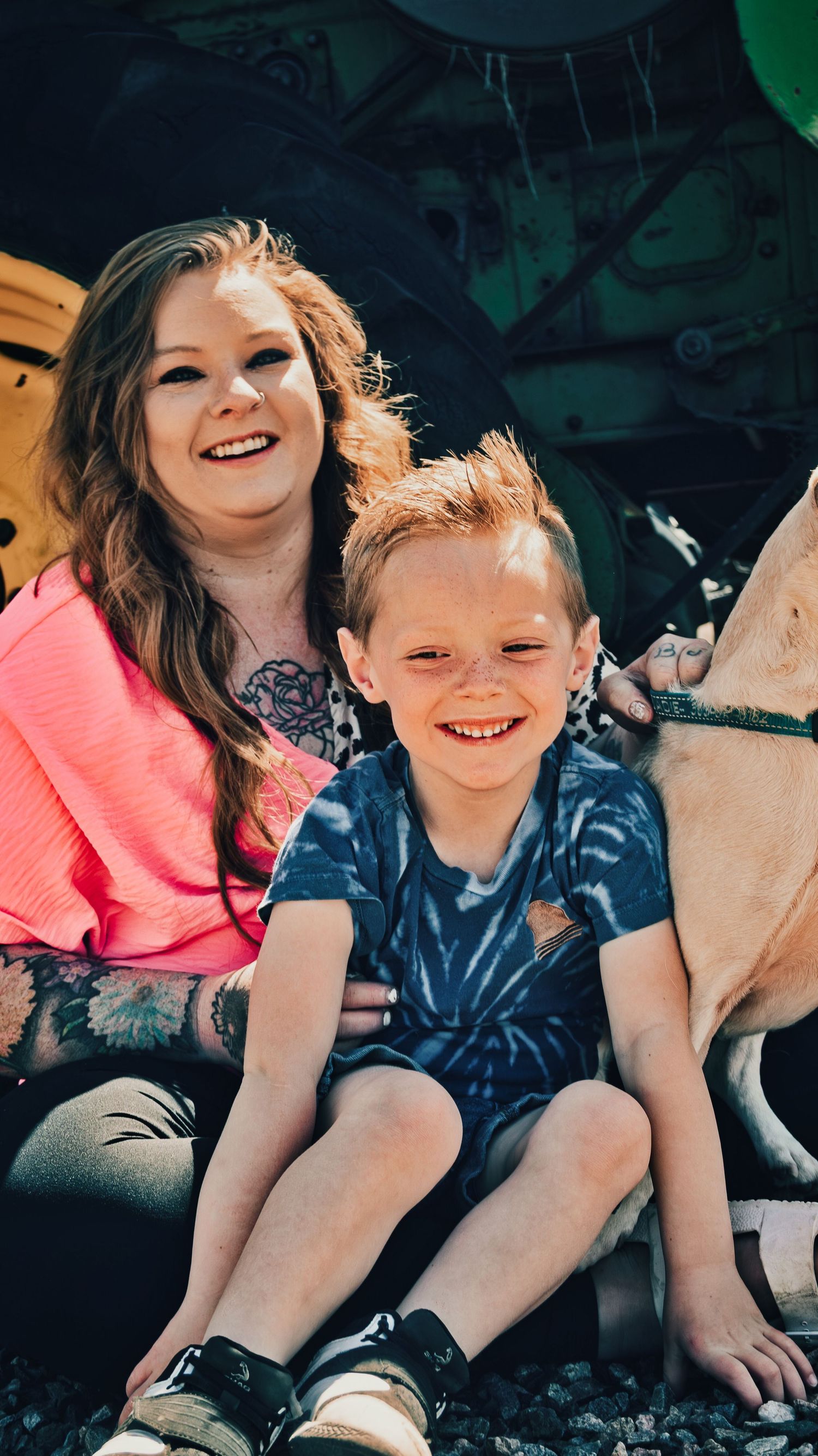 Smiling woman with tattoos and red-haired boy posing with a yellow dog outdoors. Family Photographer in Pflugerville, Tx