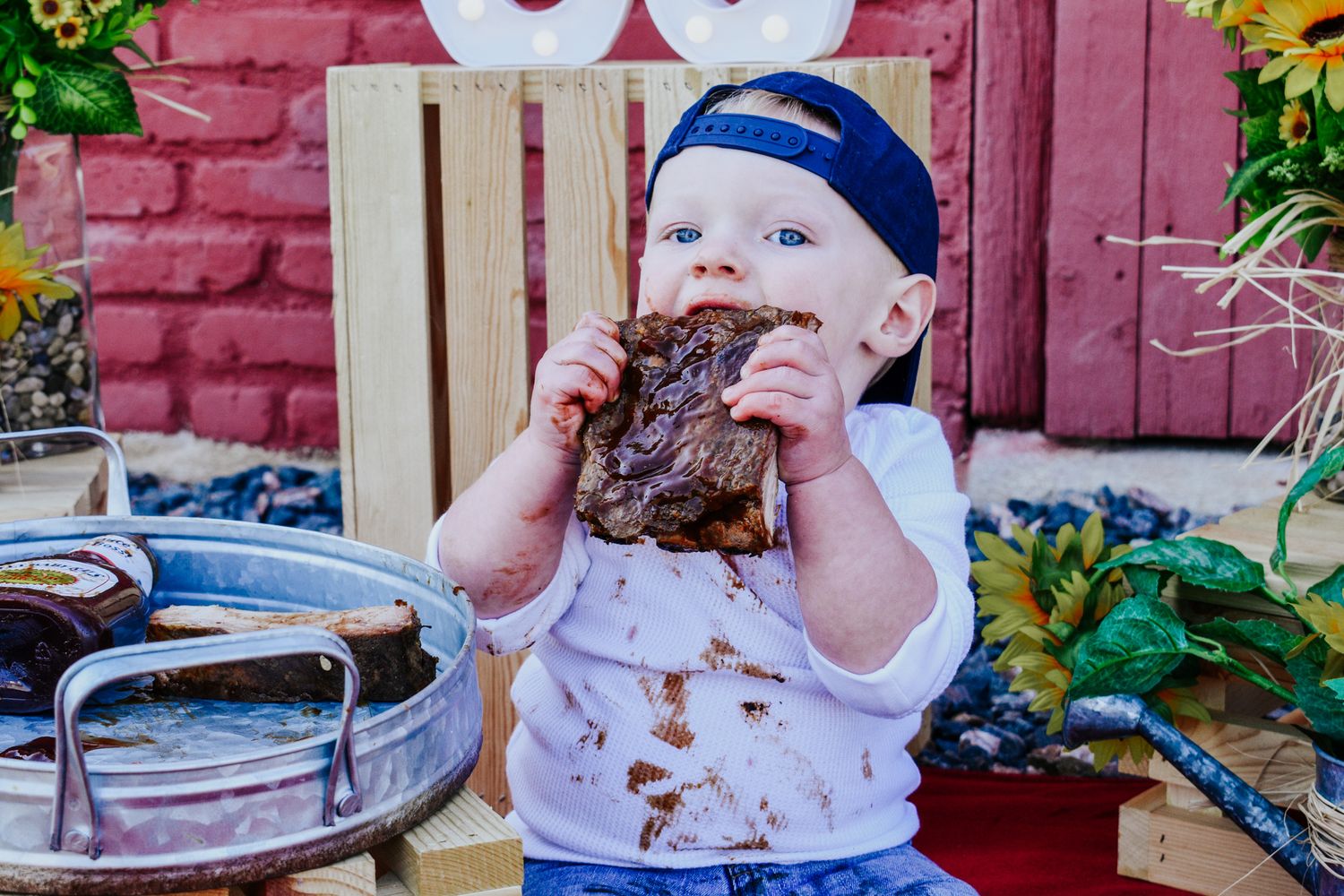 Messy baby boy eagerly eating a large piece of BBQ meat during an outdoor photo session. Family Photographer in Pflugerville, Tx
