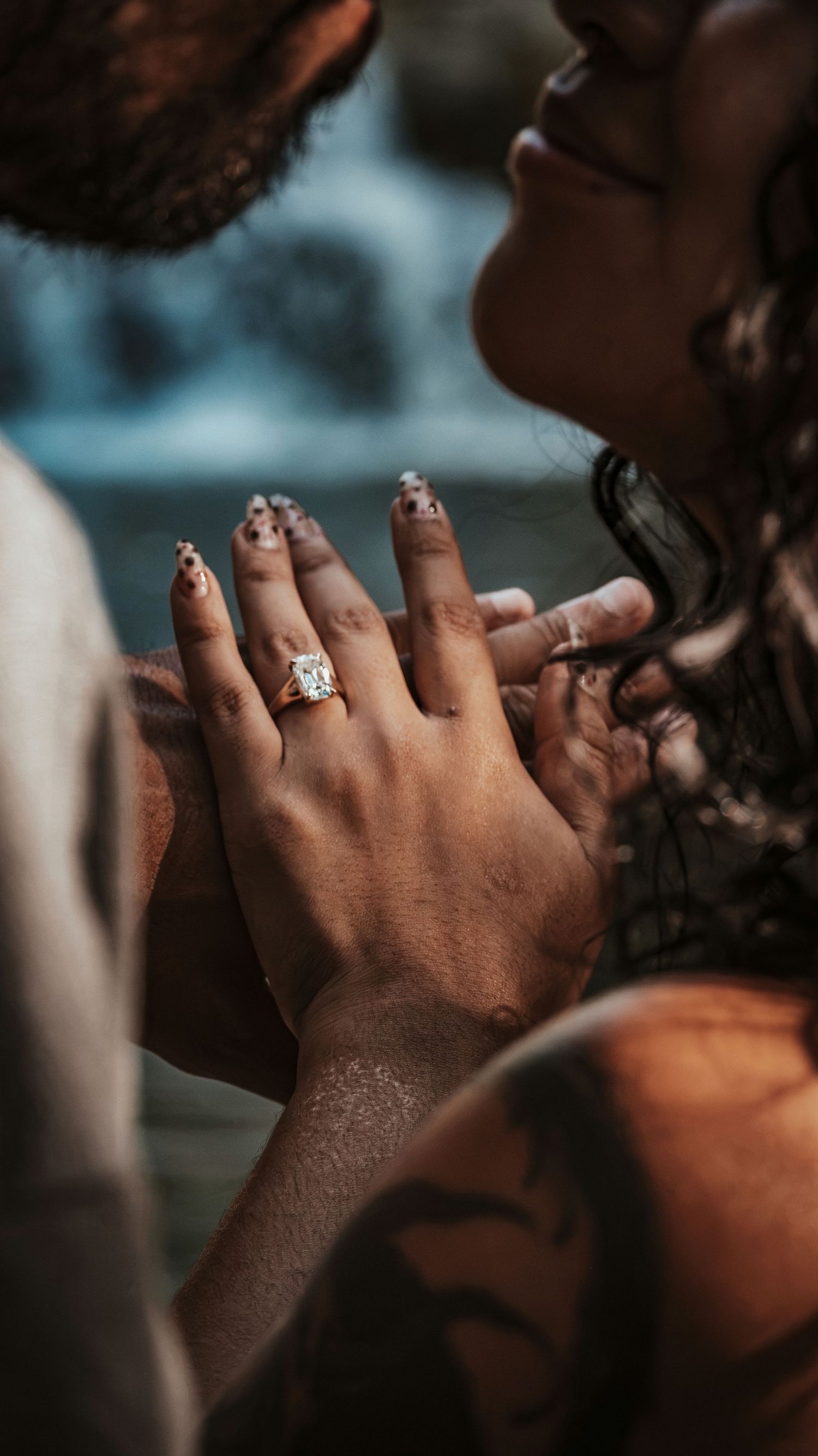 Close-up display of a sparkling diamond engagement ring while a couple shares an intimate moment for a couples session.