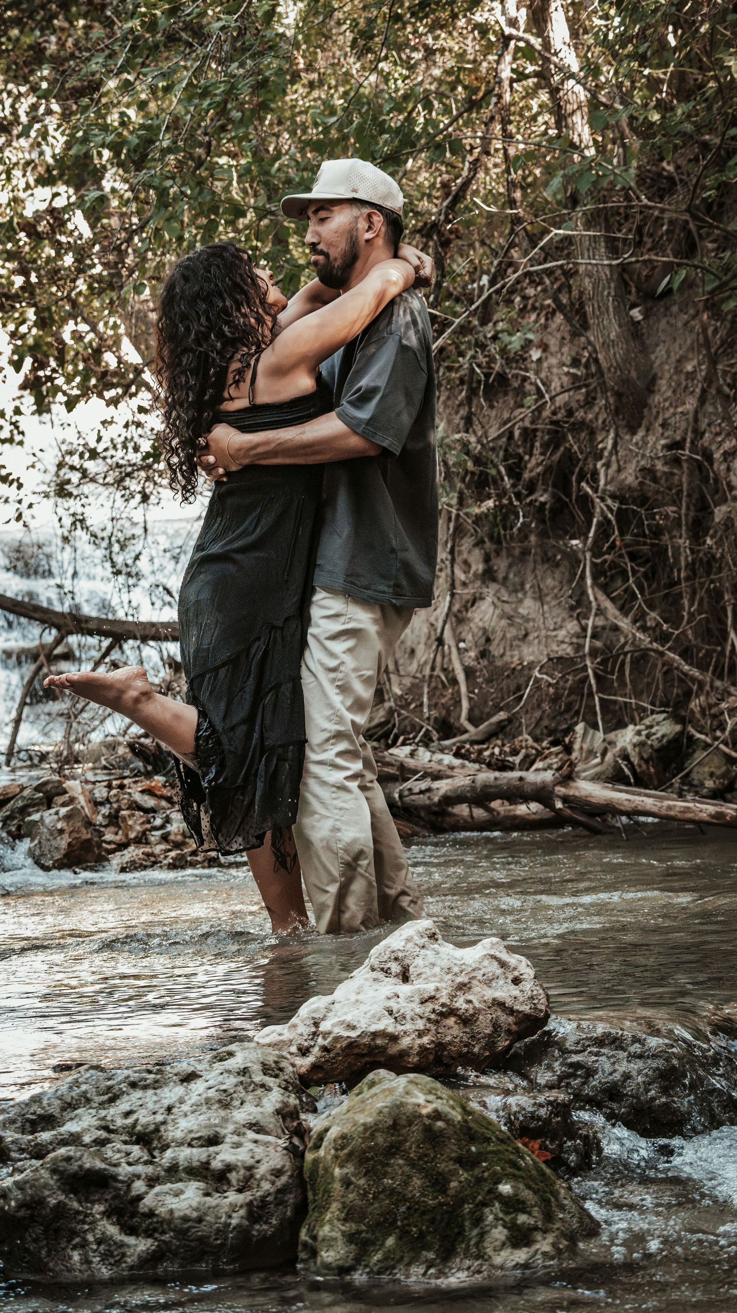 Couple embracing romantically while standing in a shallow stream surrounded by a natural setting for a couples session.