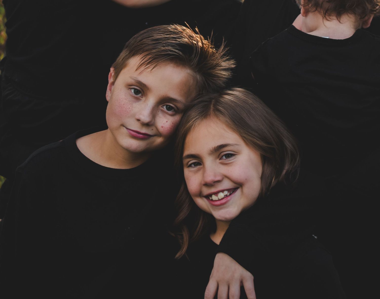Two smiling children in black tops pose together in a warm portrait photo. Family Photographer in Pflugerville, Tx