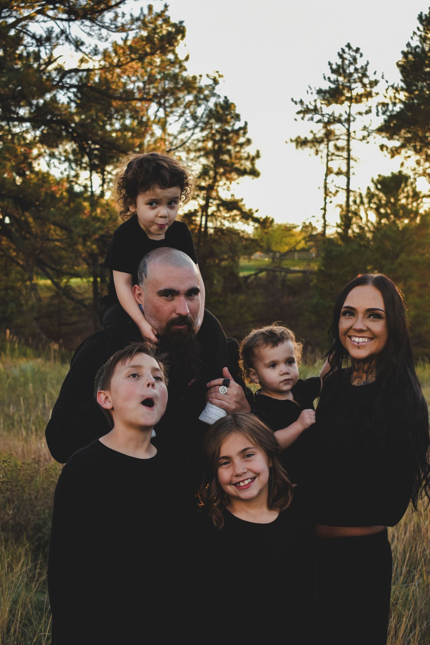 Family of six in matching black outfits laughing and posing at golden hour outdoors.