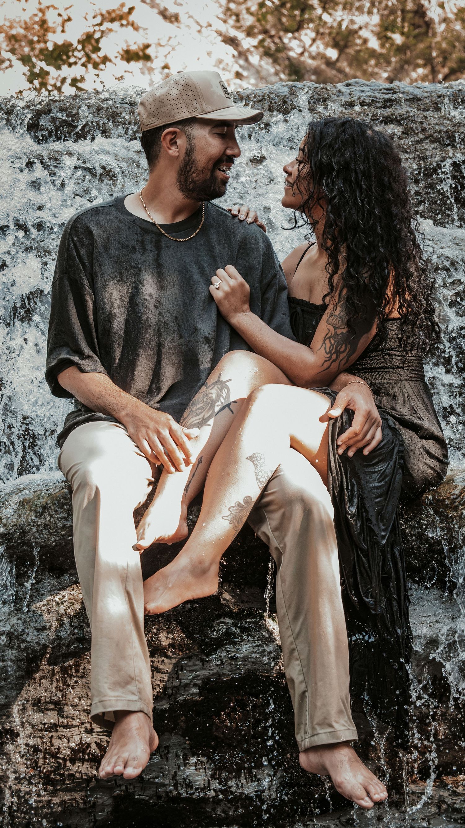 Happy couple sitting together on rocks laughing in front of a beautiful cascading waterfall outdoors.