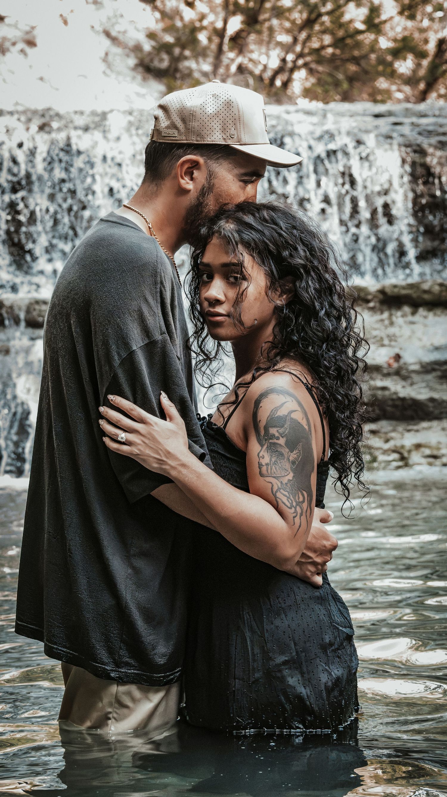 Couple standing close together in water with a waterfall behind them.
