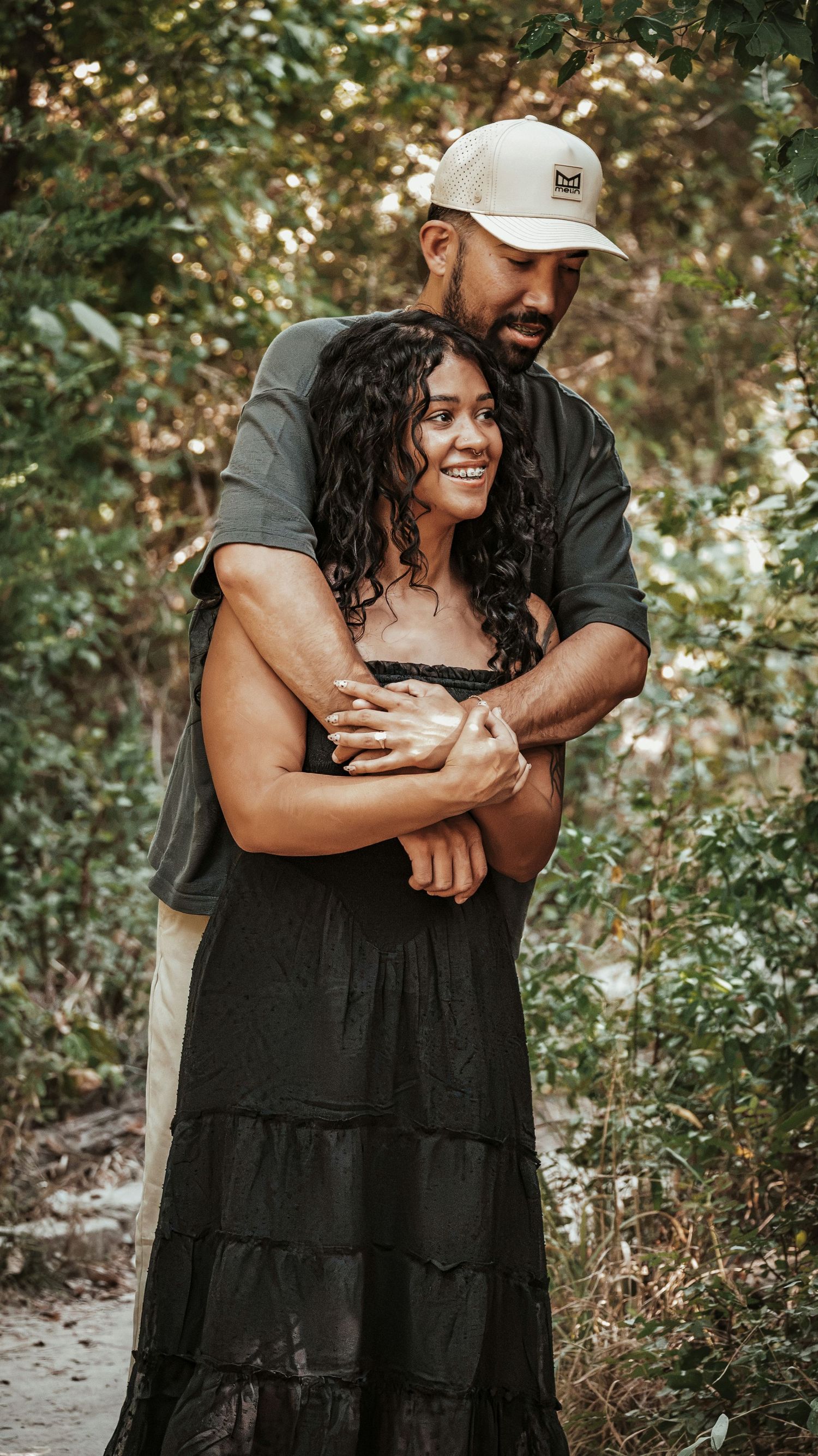 A couple embraces outdoors surrounded by lush green trees for a couples session.