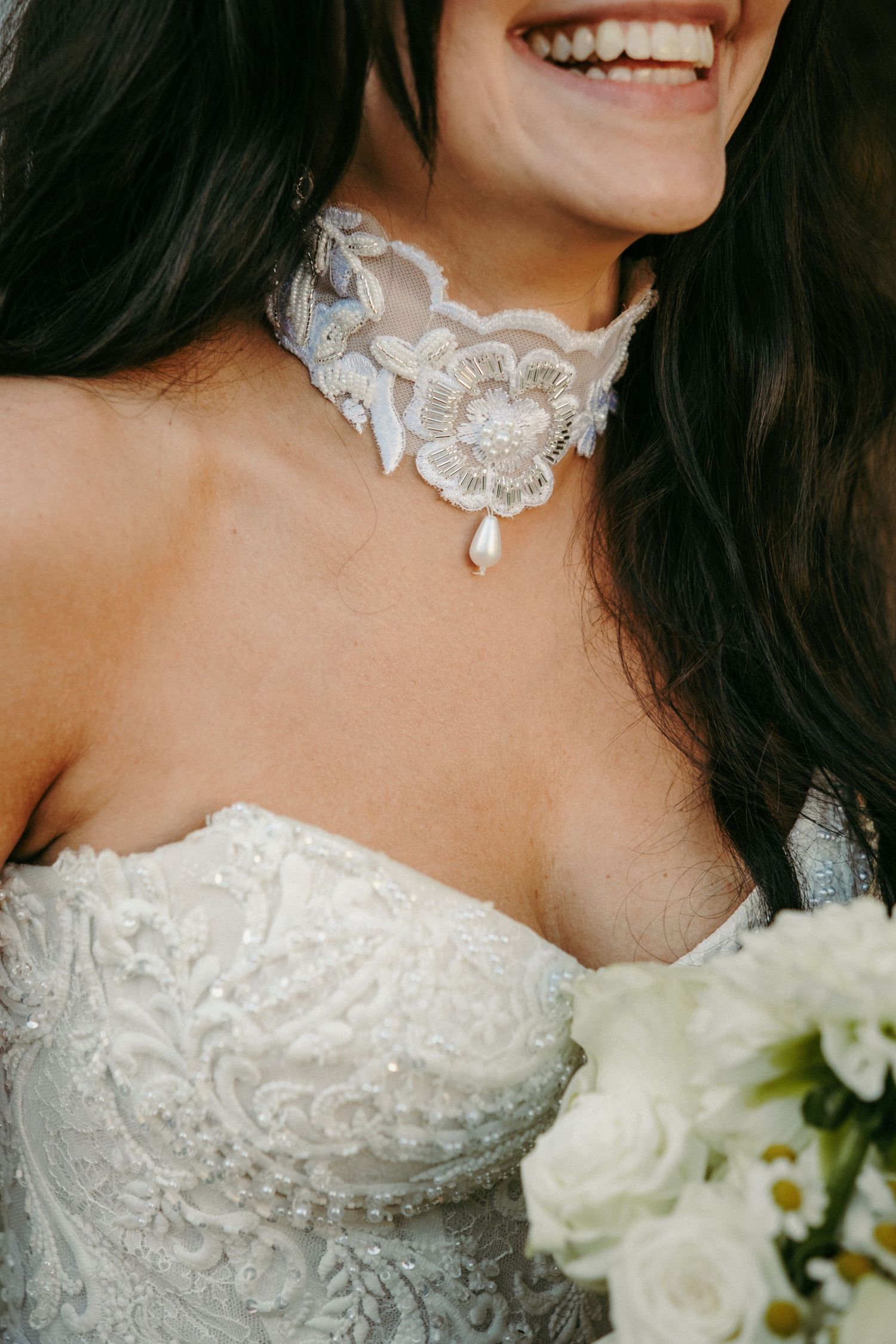 Smiling bride wearing lace choker necklace with pearl detail and beaded strapless wedding gown.
