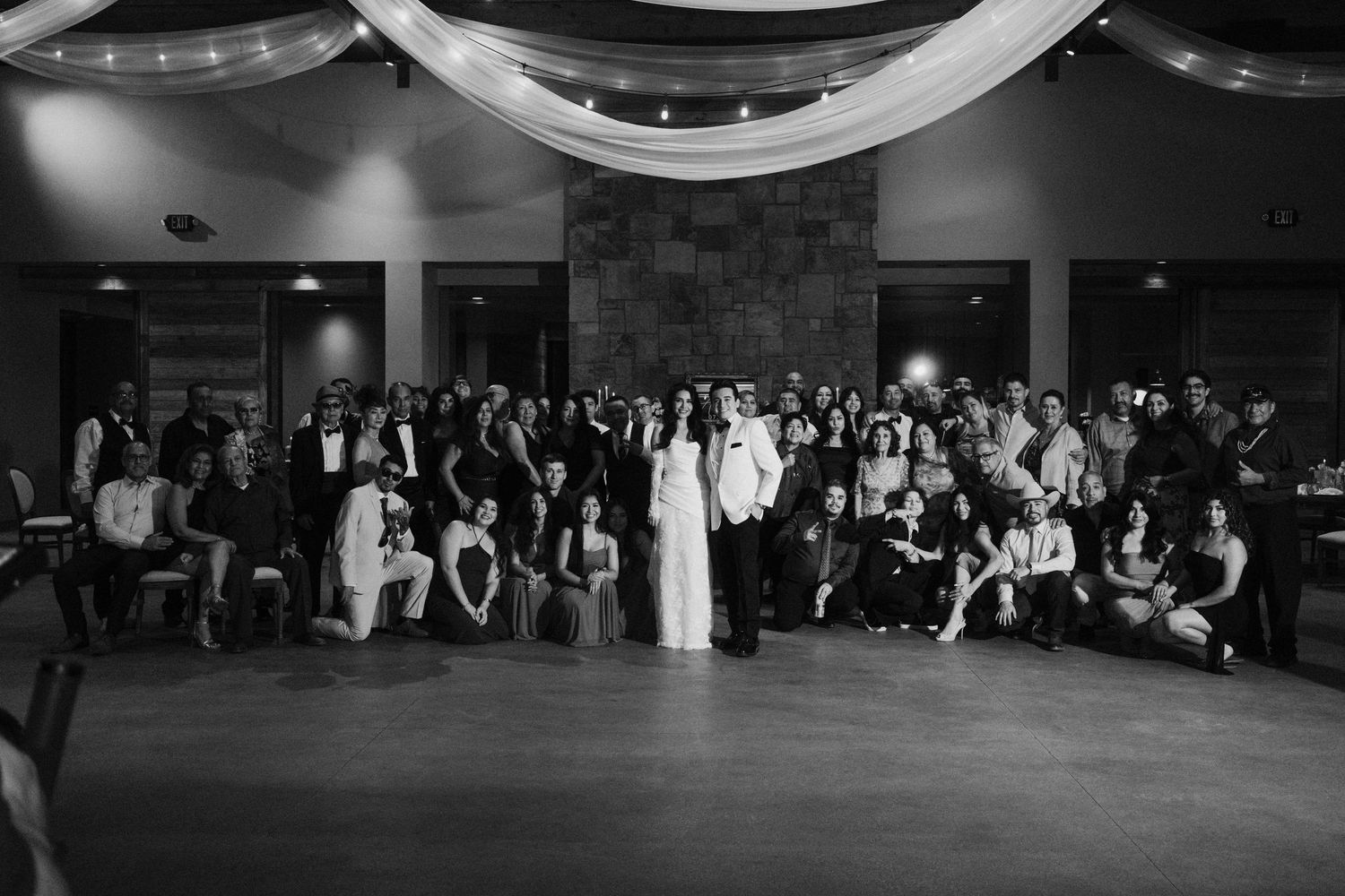 Black and white wedding reception group photo with couple and guests posing in an elegant venue.