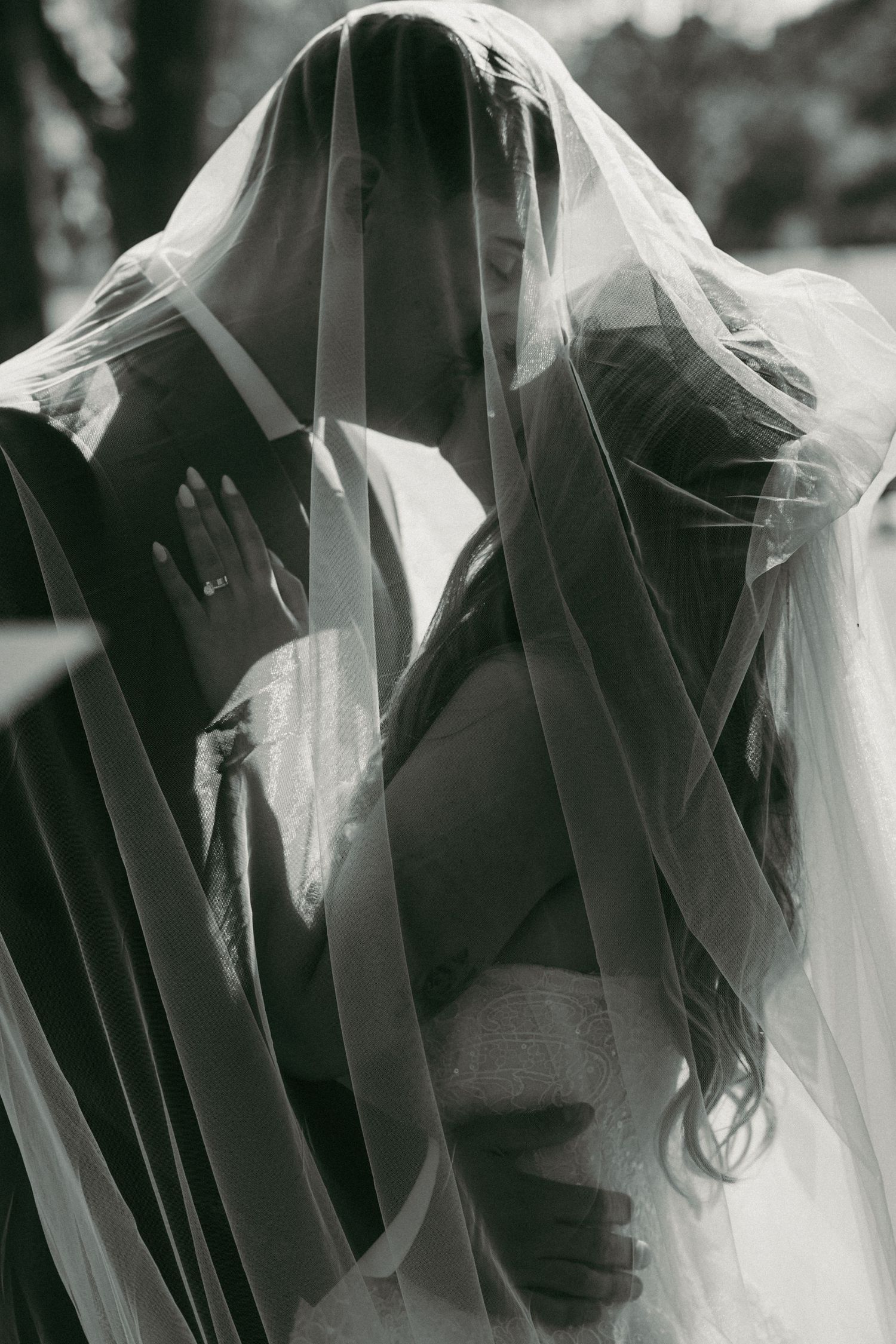 Black and white photo of bride and groom sharing intimate moment under flowing wedding veil.