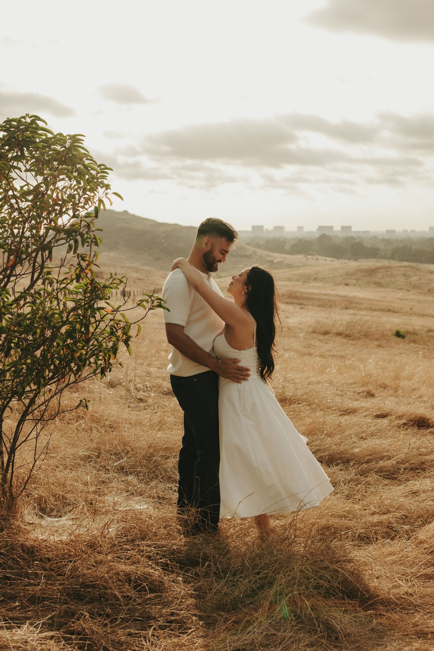 Romantic couple embracing and gazing at each other in golden dry grass field at sunset.