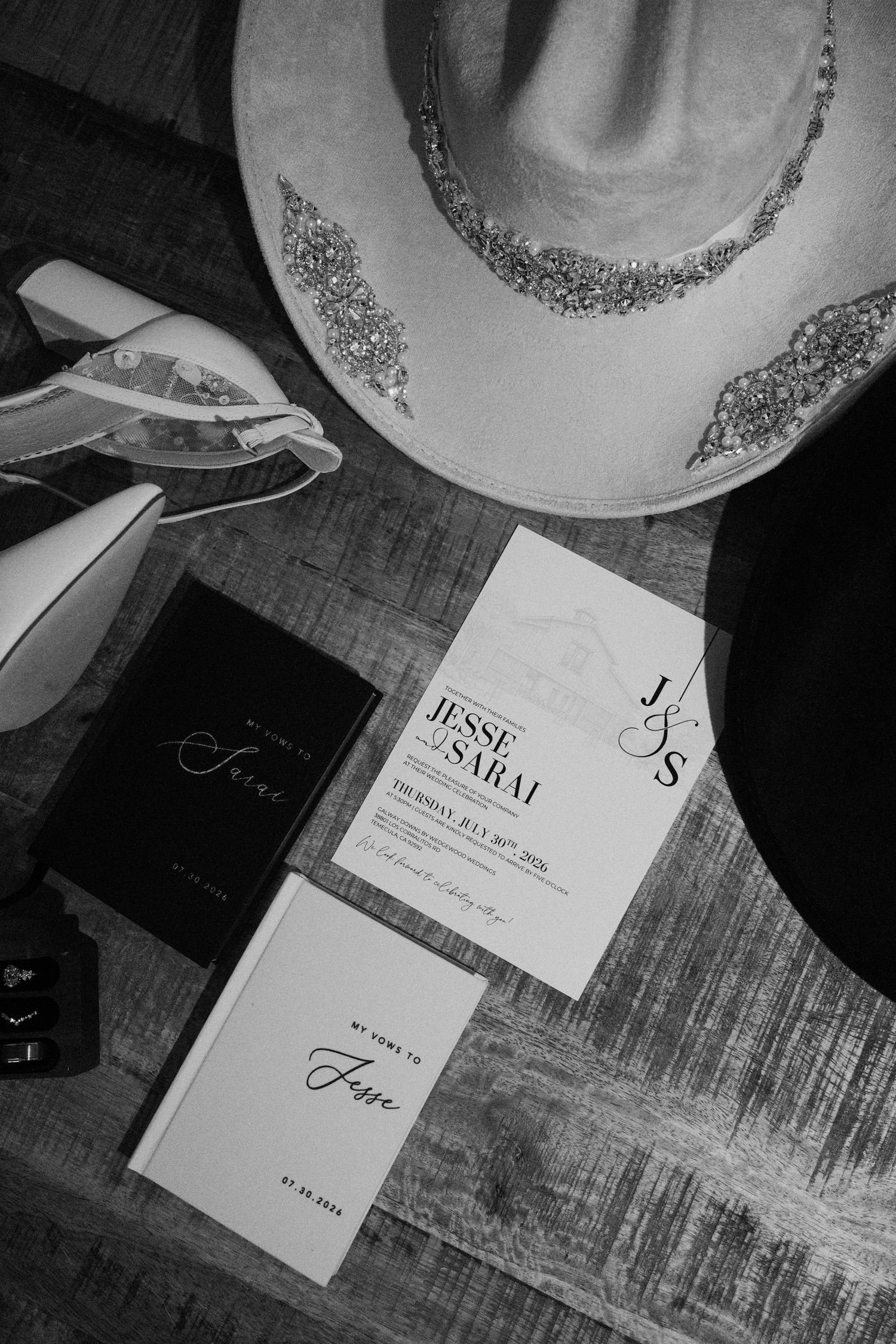 Black and white flat lay of wedding stationery for Jesse and Sarai with cowboy hat and accessories on wood surface.