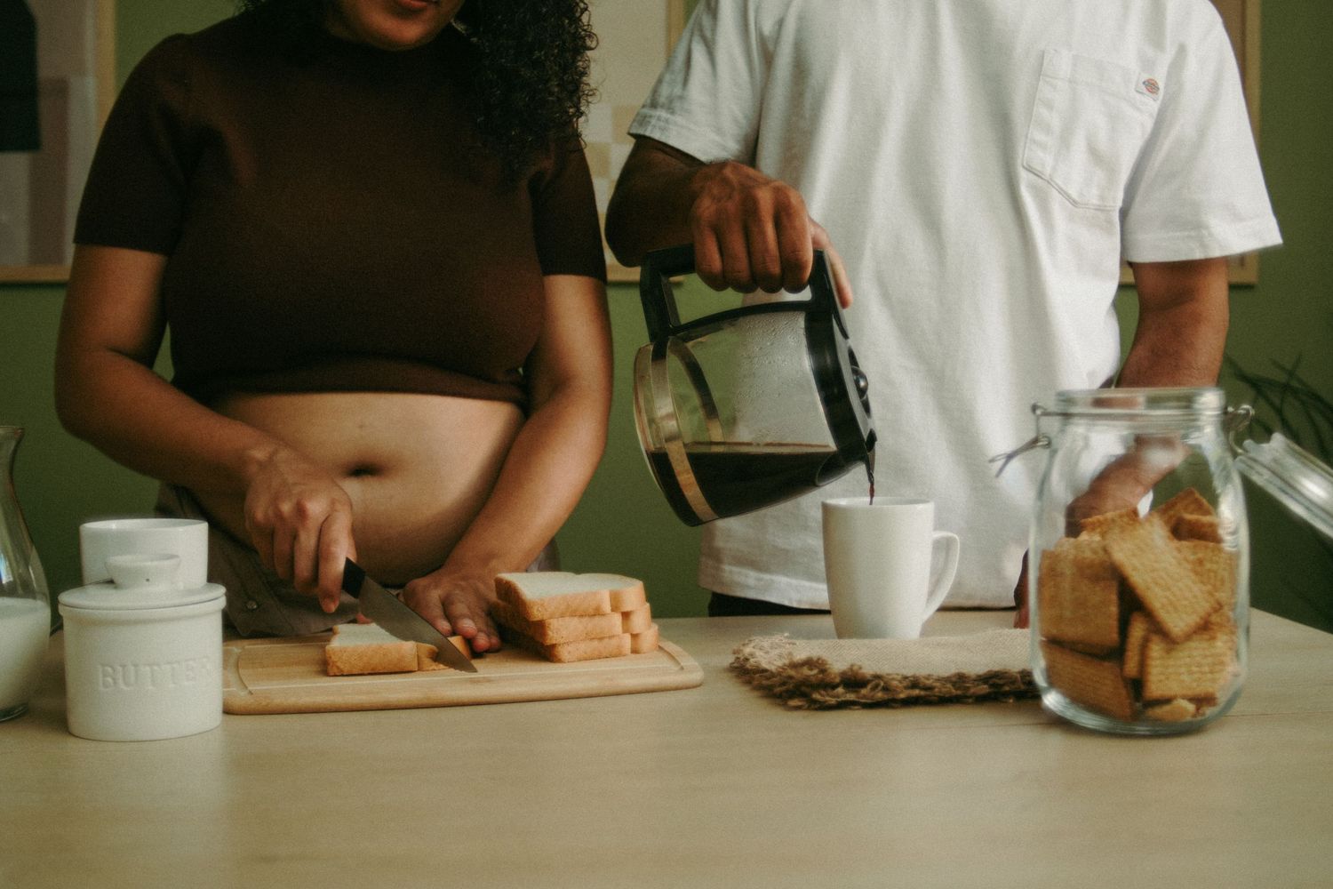 Couple preparing food and coffee together in a cozy kitchen with snacks on the counter.