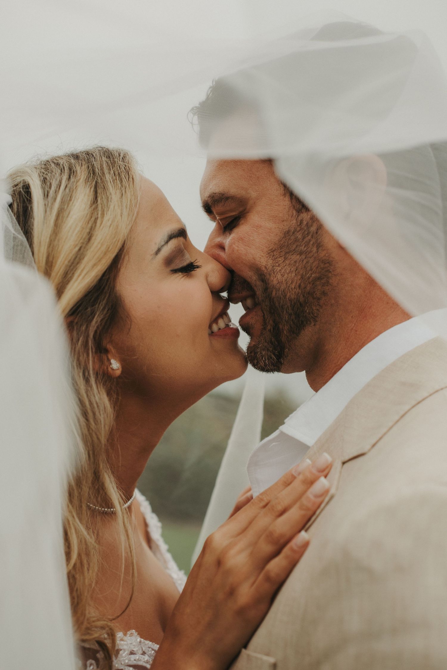 Bride and groom share a romantic kiss under a flowing white veil on their wedding day.