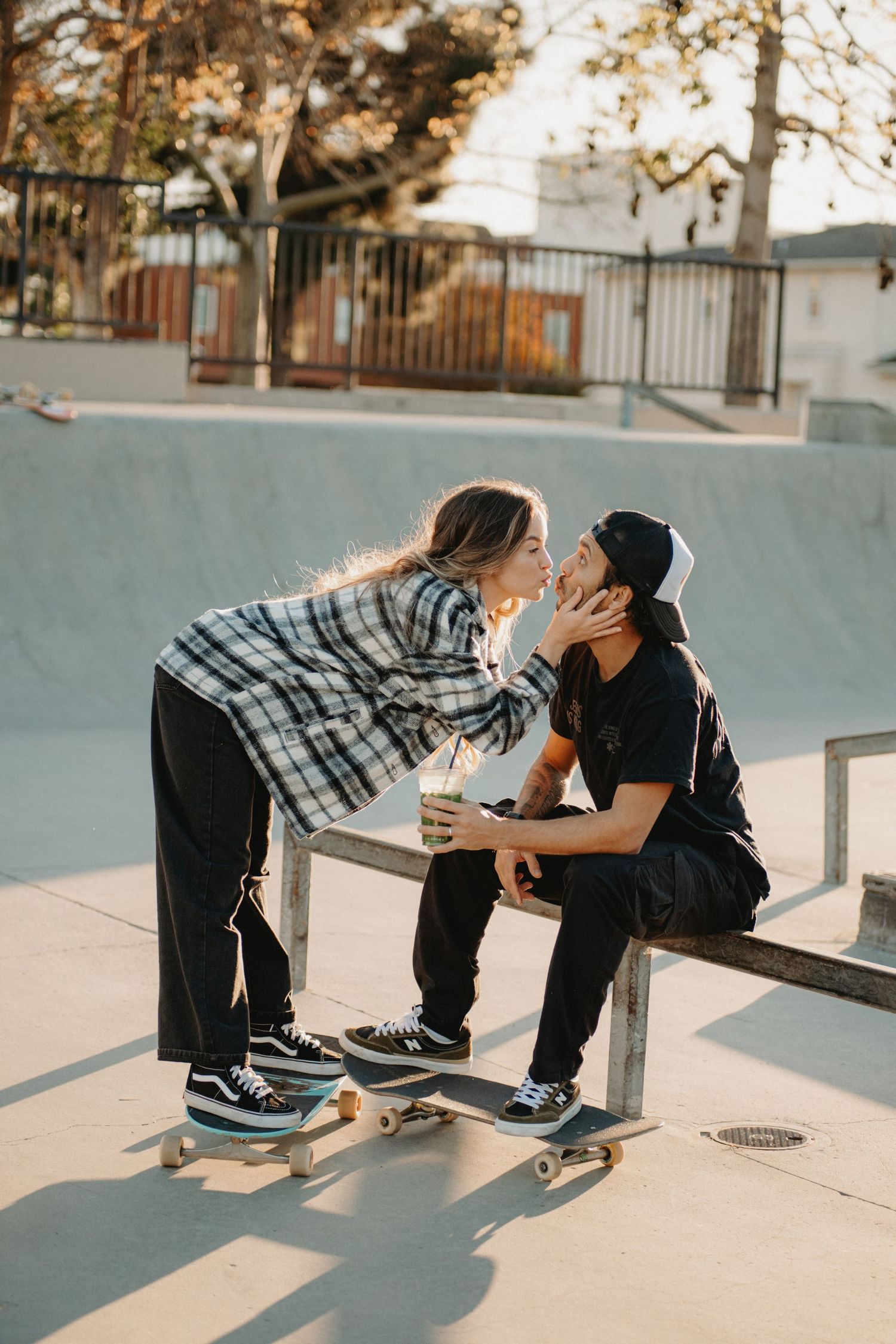 Couple sharing a romantic kiss at a skate park, with skateboards and concrete ramps in the background.