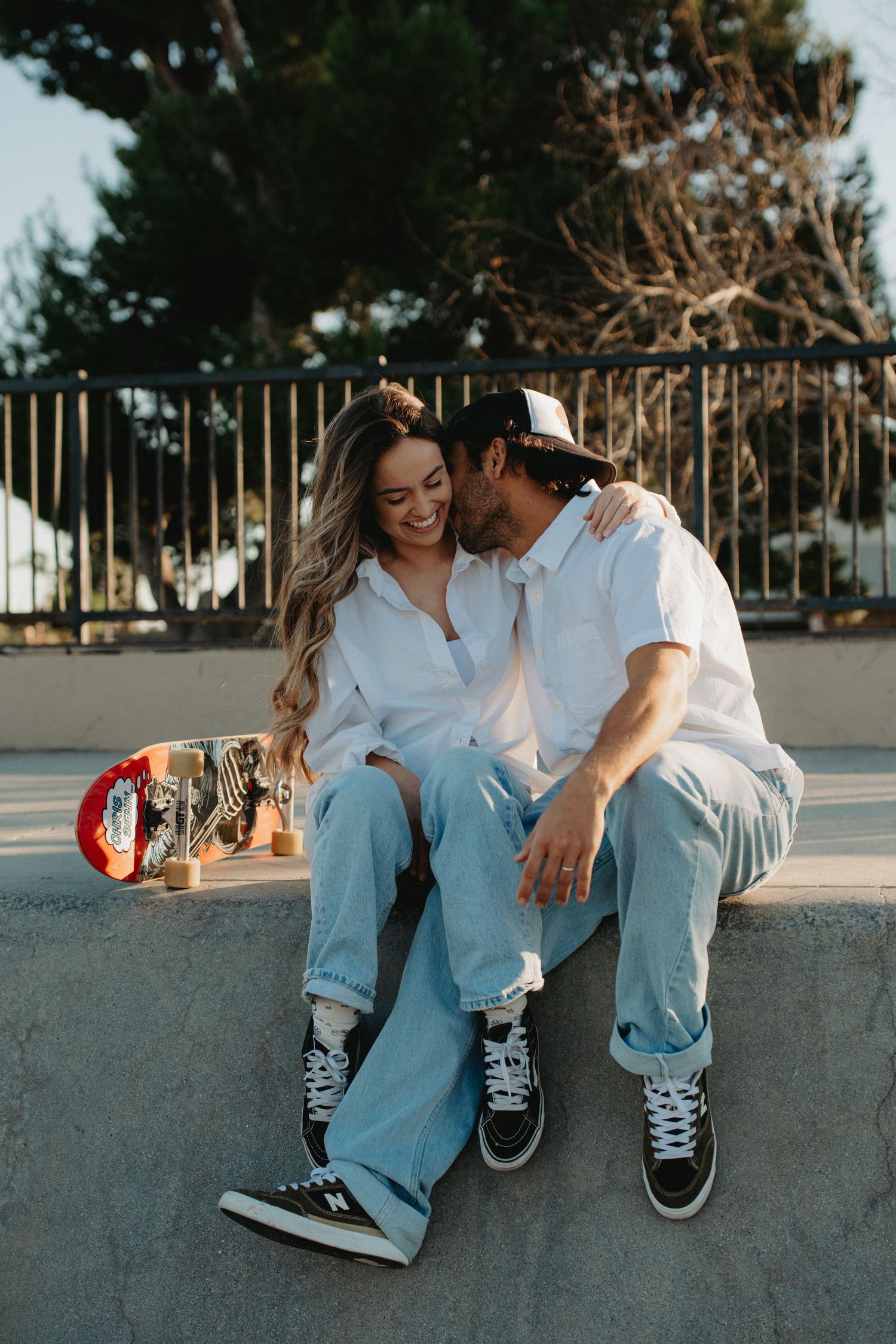 Couple sitting together at a skate park, wearing matching white shirts and light blue jeans with Vans sneakers.