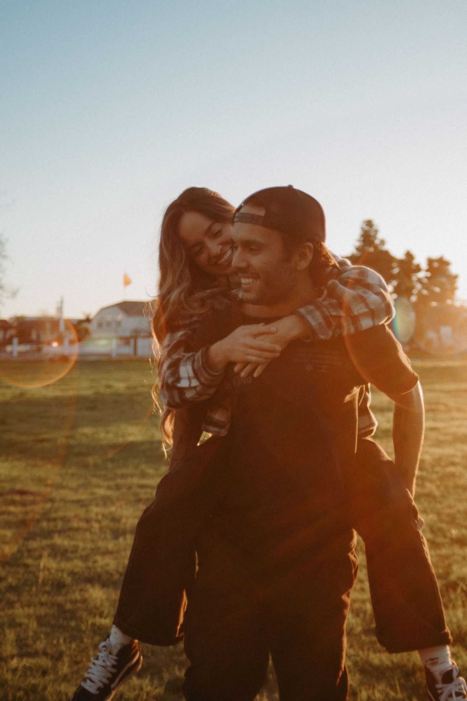 Happy couple sharing a piggyback ride in a sunny field at golden hour.