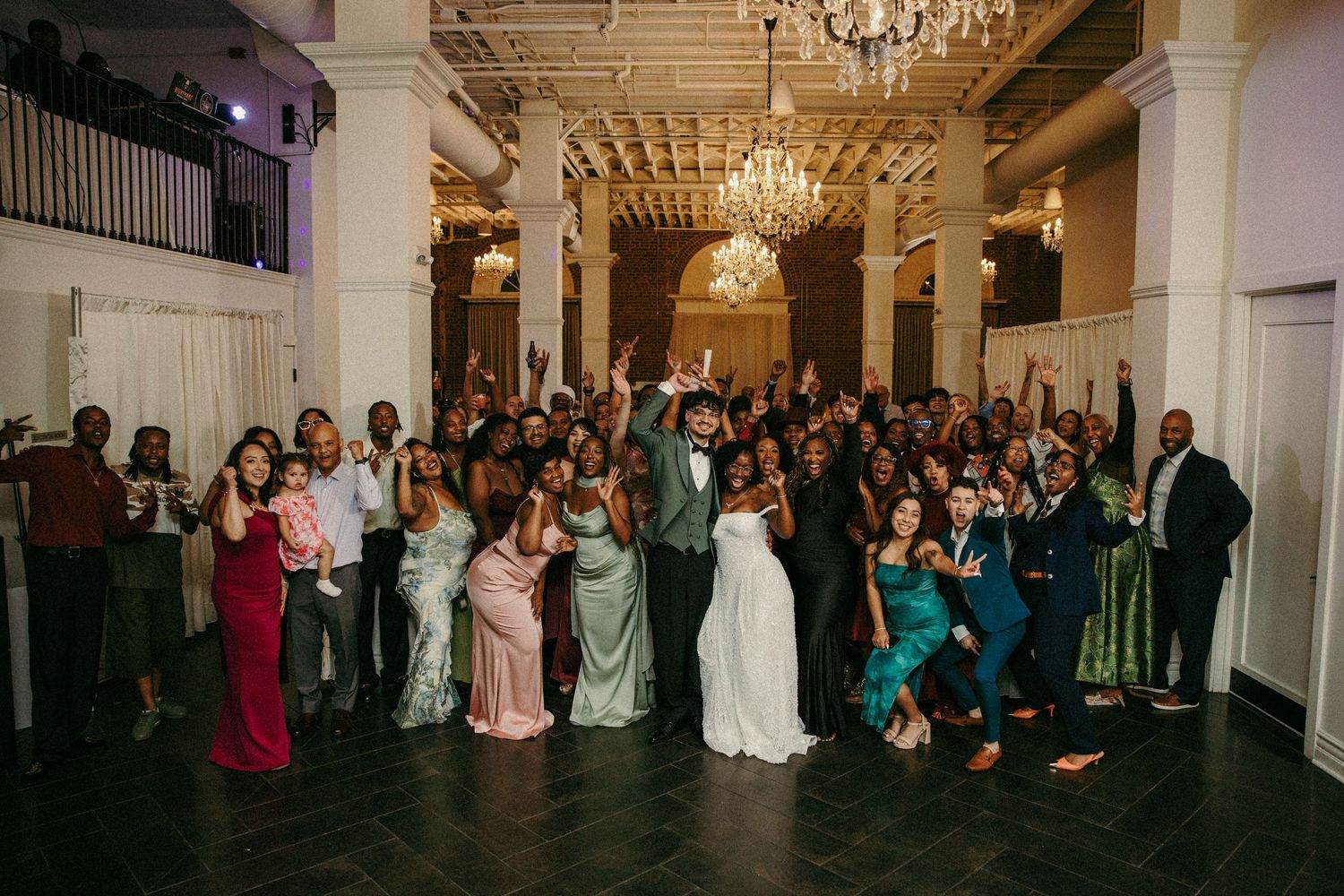 Wedding party and guests celebrate together in elegant chandelier ballroom.