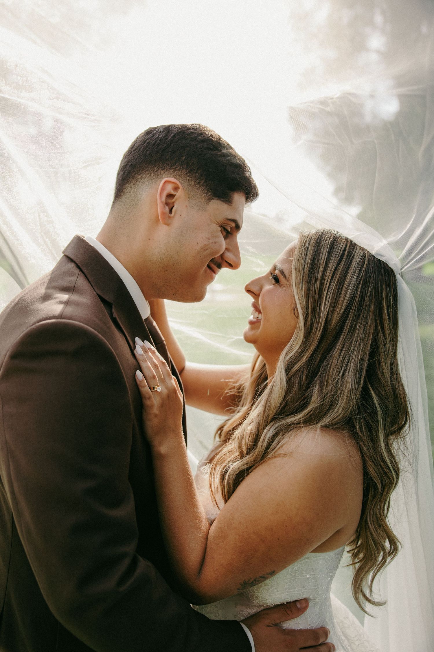 A bride and groom share a romantic moment under a flowing veil, gazing lovingly at each other on their wedding day.