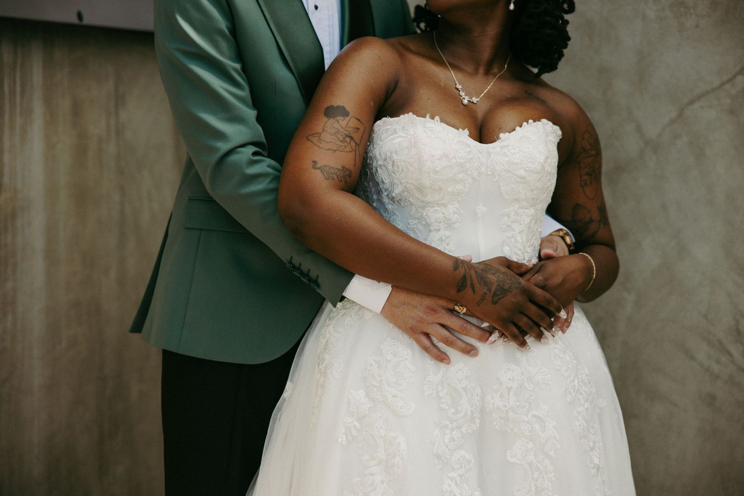 Bride in strapless white lace ball gown embraced by groom in green tuxedo jacket at wedding ceremony.