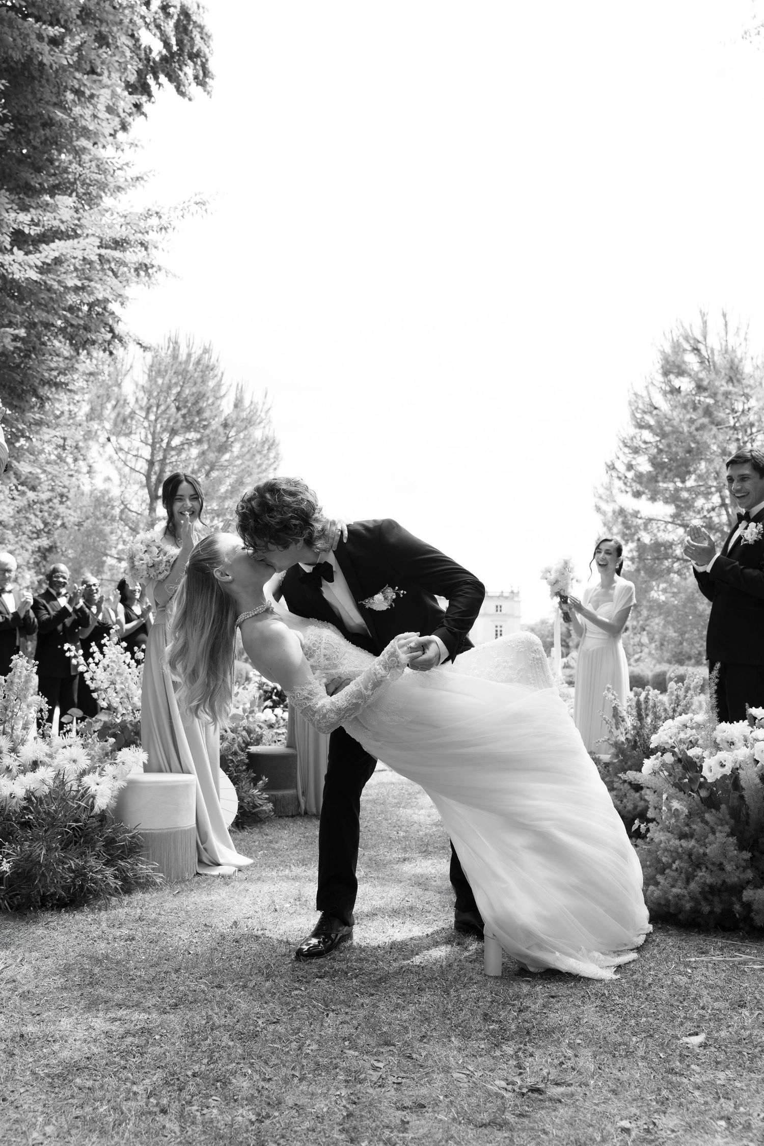 Black and white photo of a groom dipping his bride for a kiss after their outdoor wedding ceremony.