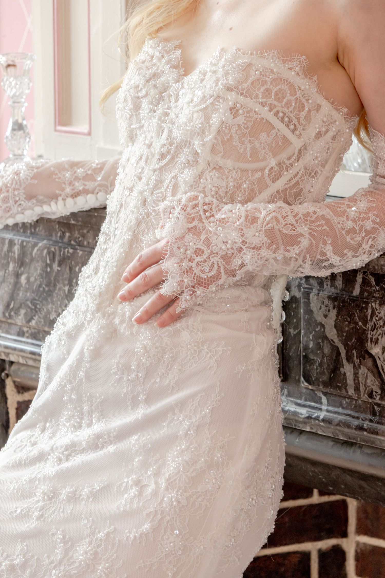 Close-up of a bride in an elegant strapless lace wedding gown with sheer long sleeves and intricate beaded detailing.