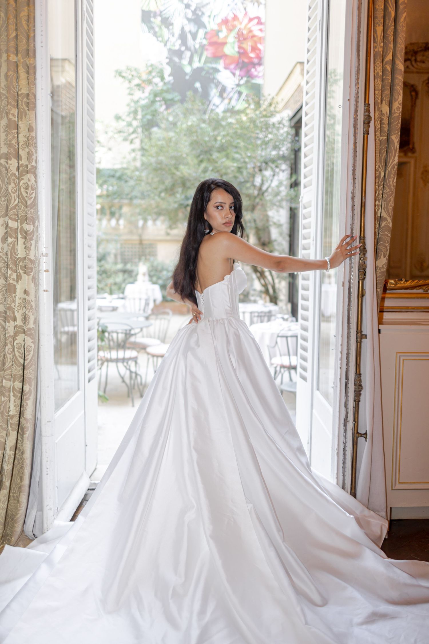 Elegant bride in a strapless satin ballgown with dramatic train standing in ornate French château doorway.