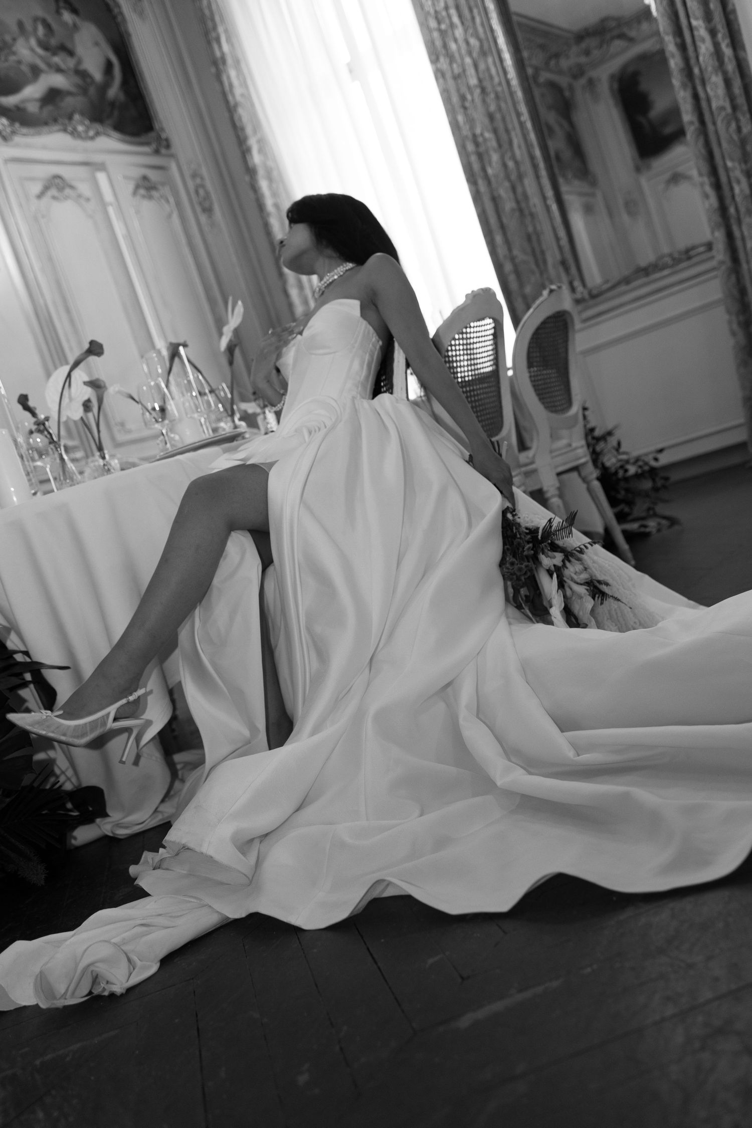 Black and white photo of bride in strapless wedding gown with high slit in ornate room.
