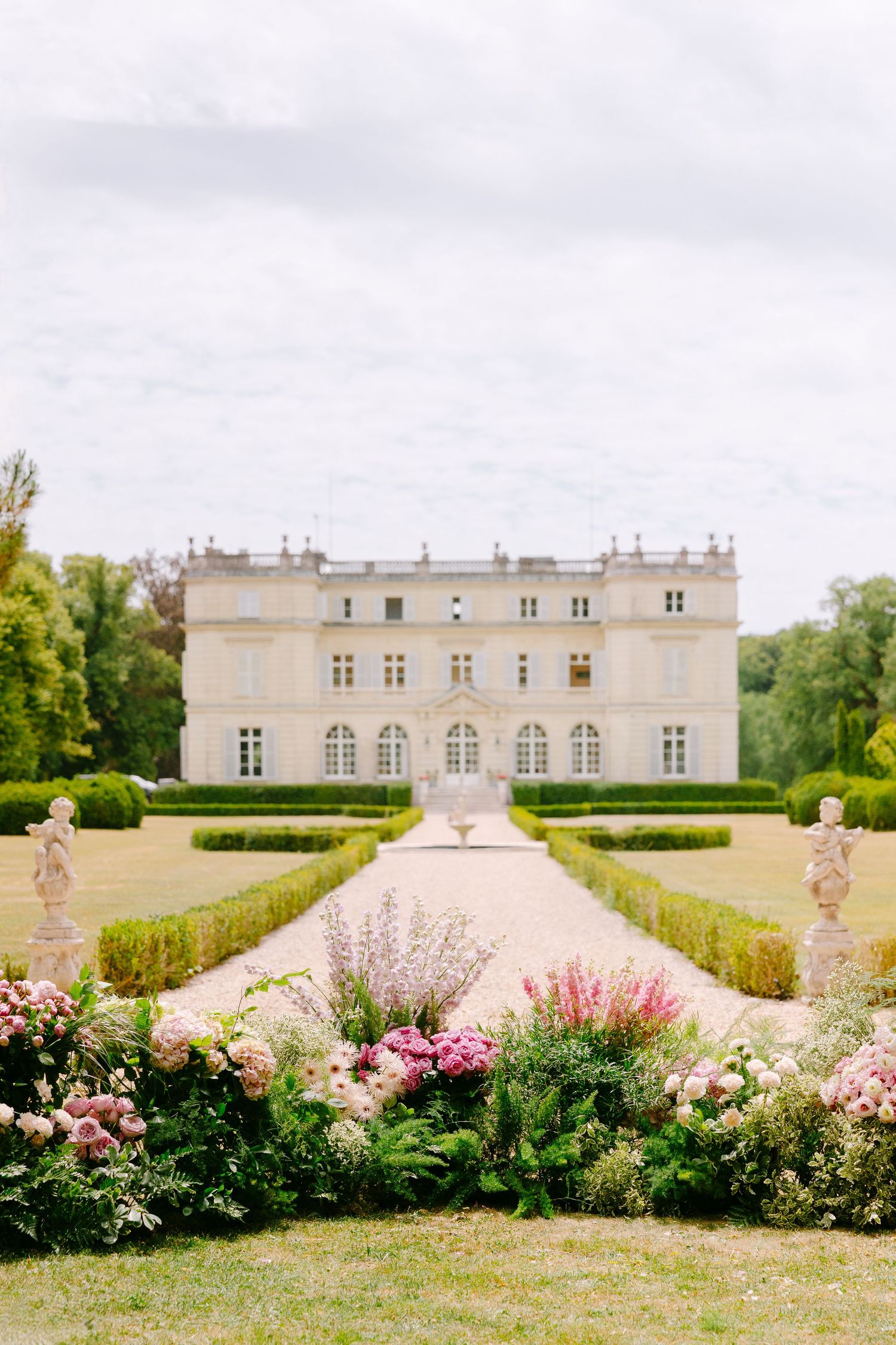 Grand French chateau wedding venue with manicured gardens and pink floral arrangements lining pathway.