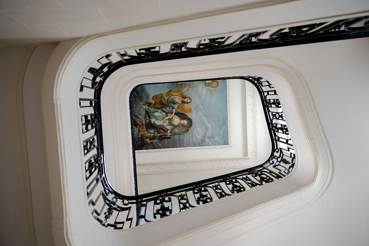 Aerial view of an elegant spiral staircase with black and white railing and a classical painting visible below.