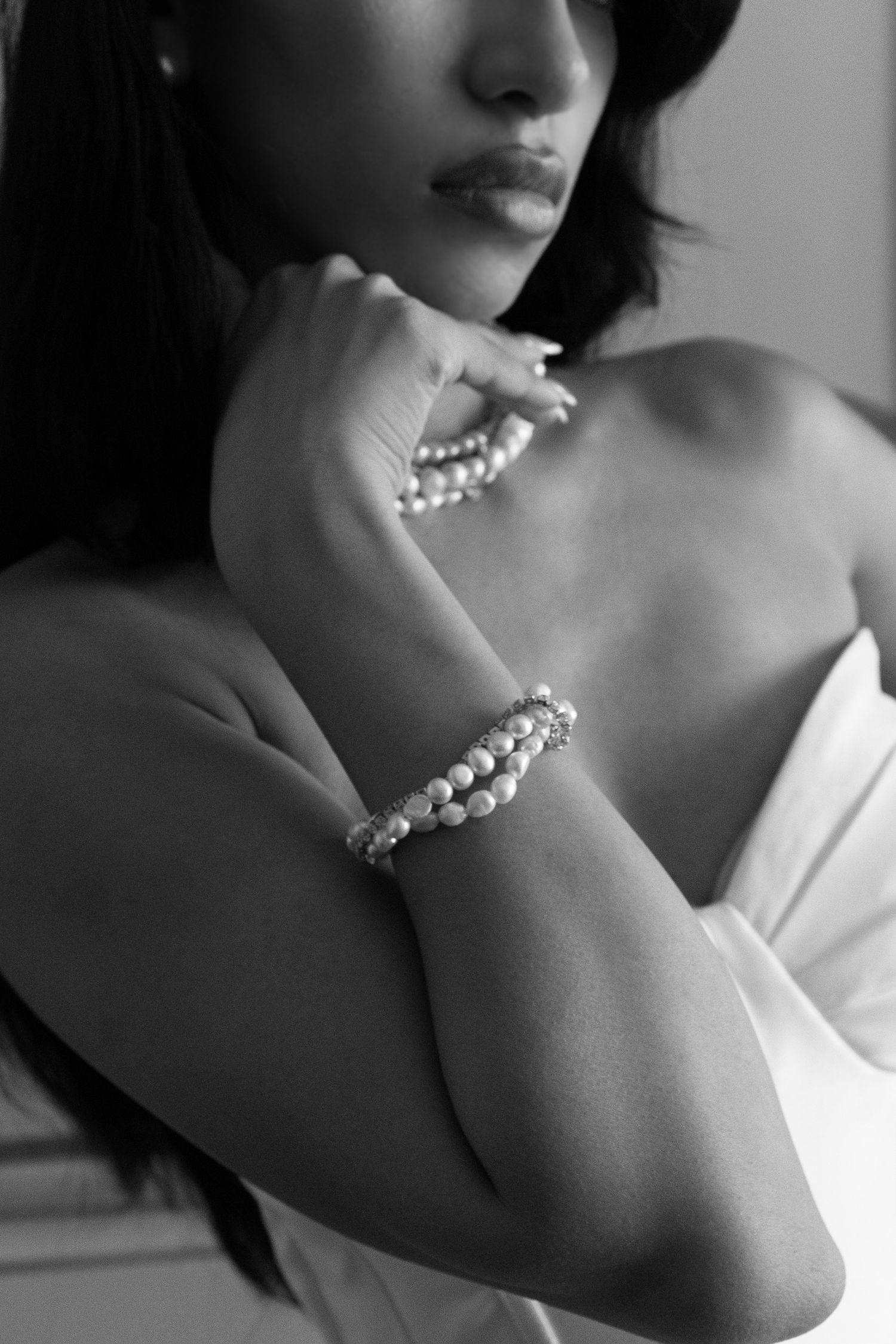 Black and white photo of a woman wearing elegant pearl bracelets and necklace in a strapless white dress.
