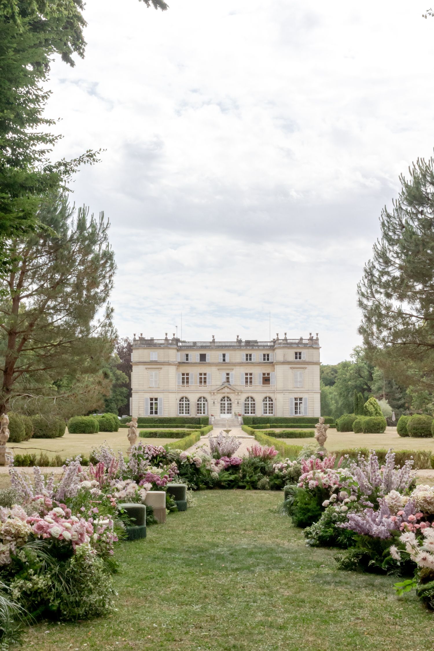Grand French chateau wedding venue with romantic pink and lavender floral ceremony aisle on manicured lawn.