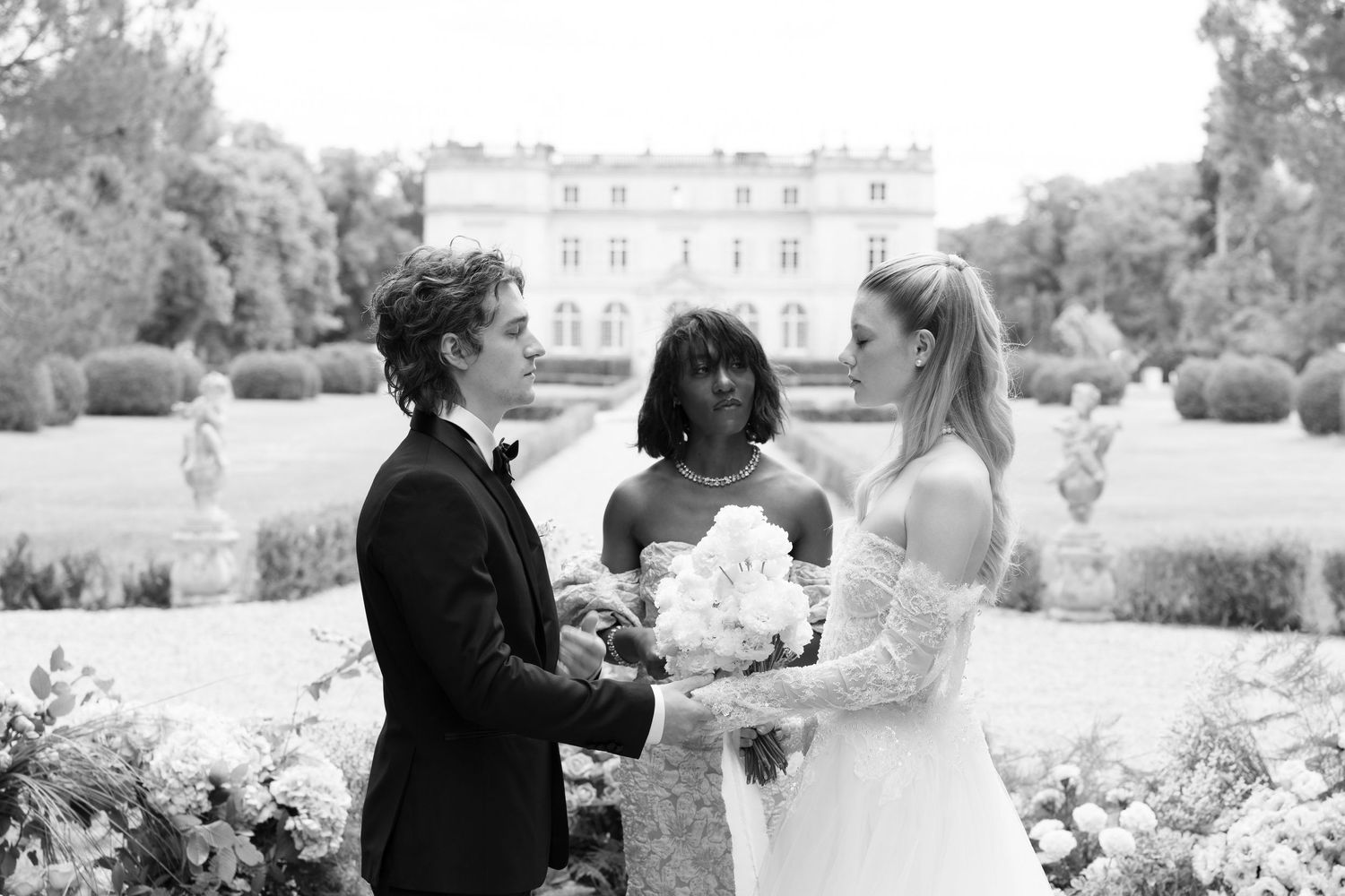 Black and white photo of a couple exchanging vows with an officiant at an elegant outdoor wedding ceremony.