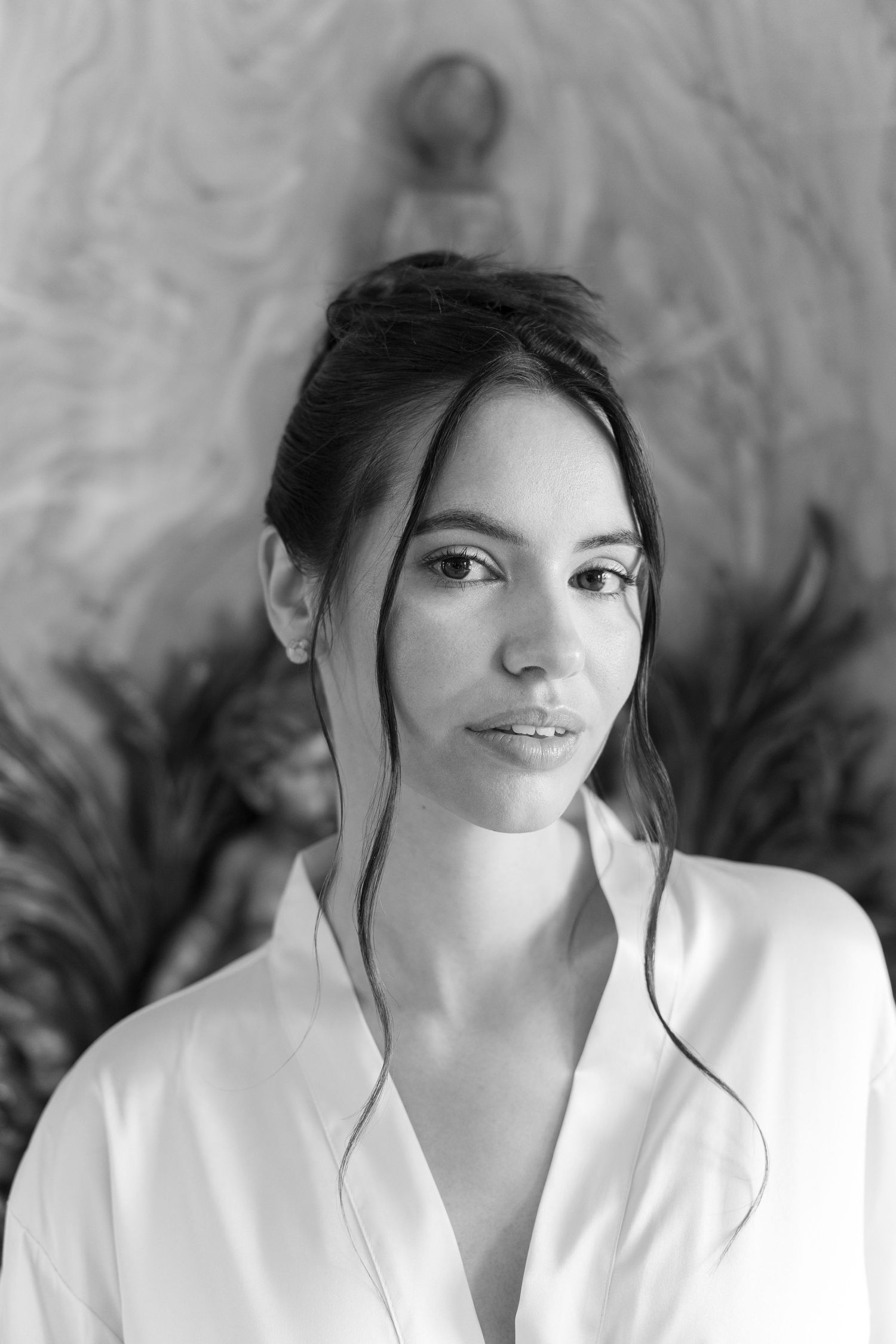 Black and white portrait of a young woman in a white shirt with elegant updo hairstyle against decorative background.