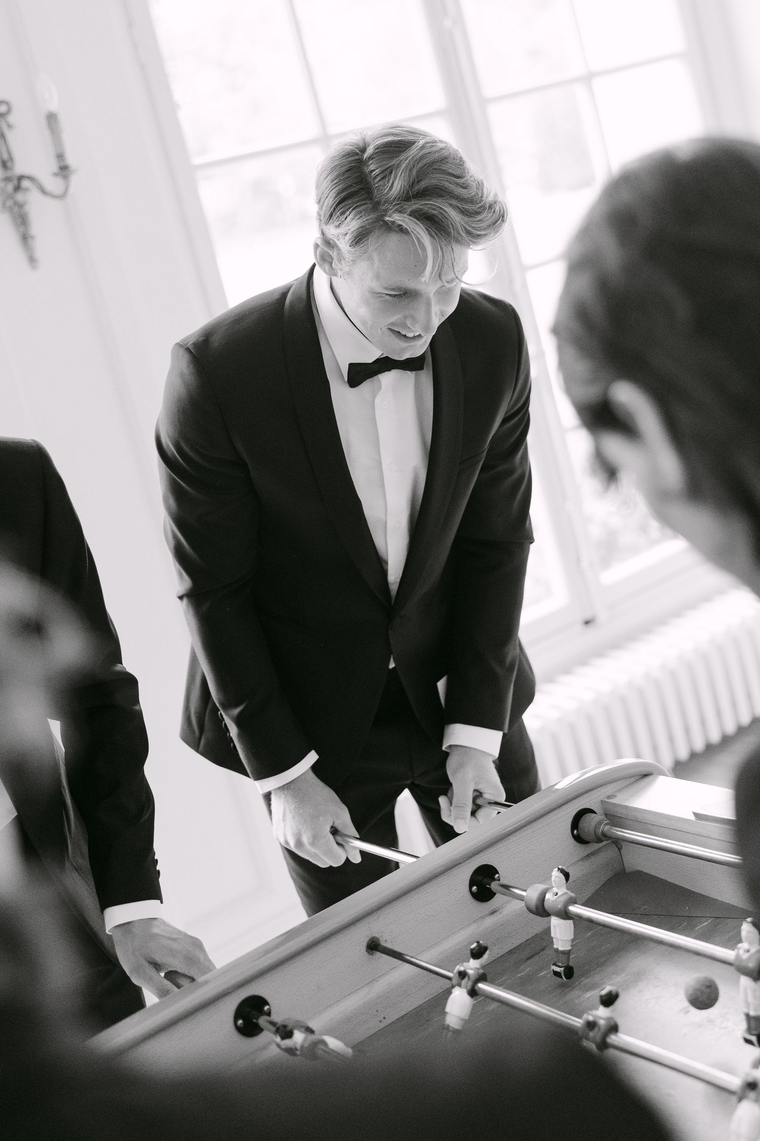 Man in tuxedo playing foosball with friends in black and white photo.