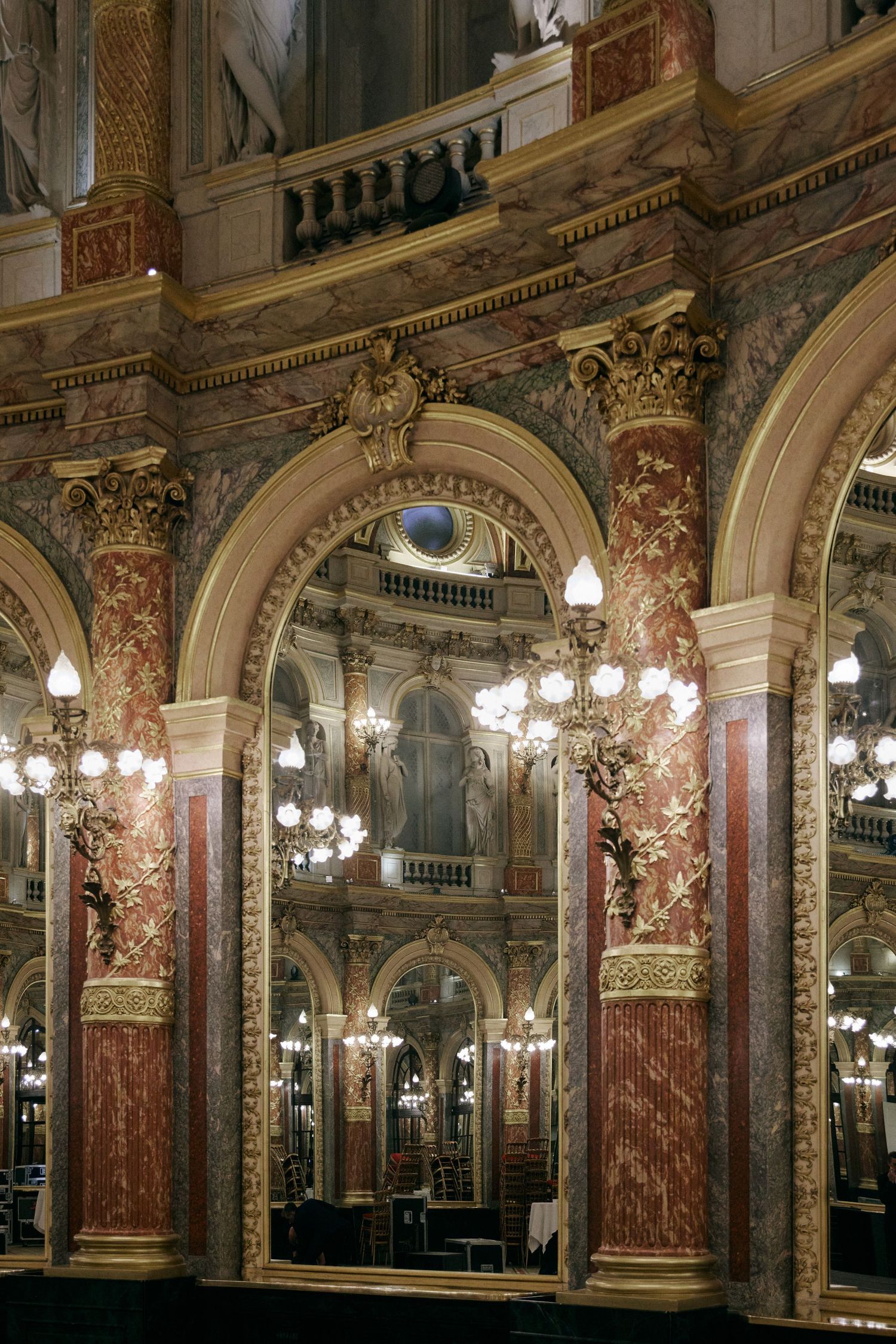 Ornate interior of a grand opera house featuring gilded arches, red marble columns, and elegant chandeliers.