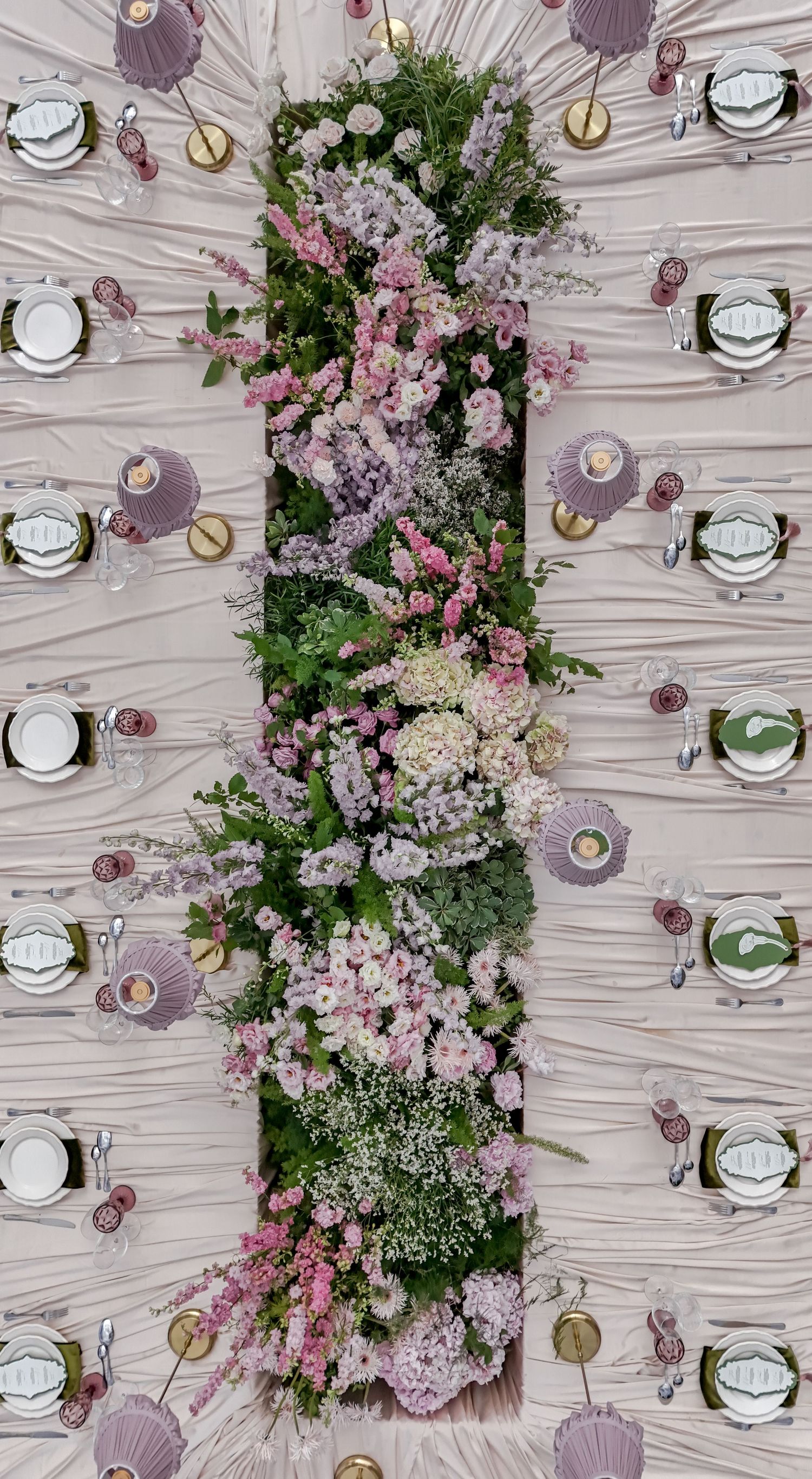 Aerial view of an elegant wedding table with a lush floral centerpiece of pink and white blooms, set with lavender place settings.