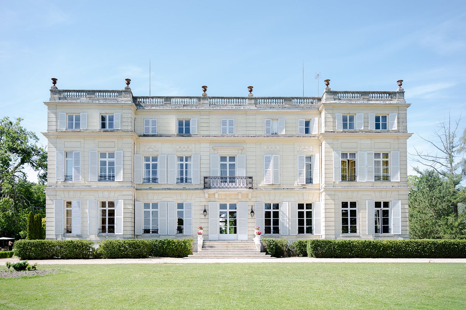 Elegant white French château with symmetrical façade, tall windows, and manicured hedges on a lush green lawn.