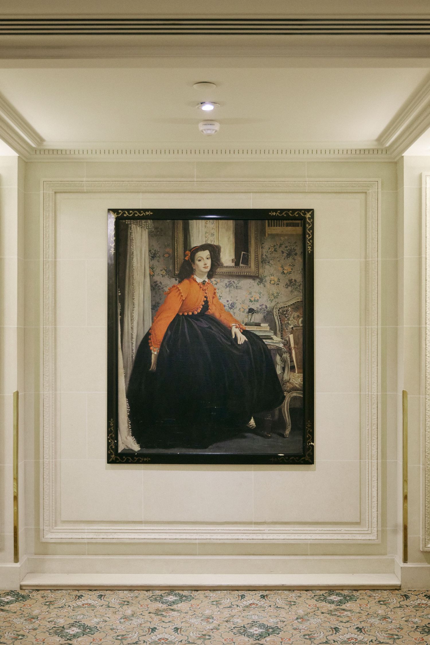 Victorian portrait painting of a woman in orange jacket and black dress displayed in an elegant hotel corridor.