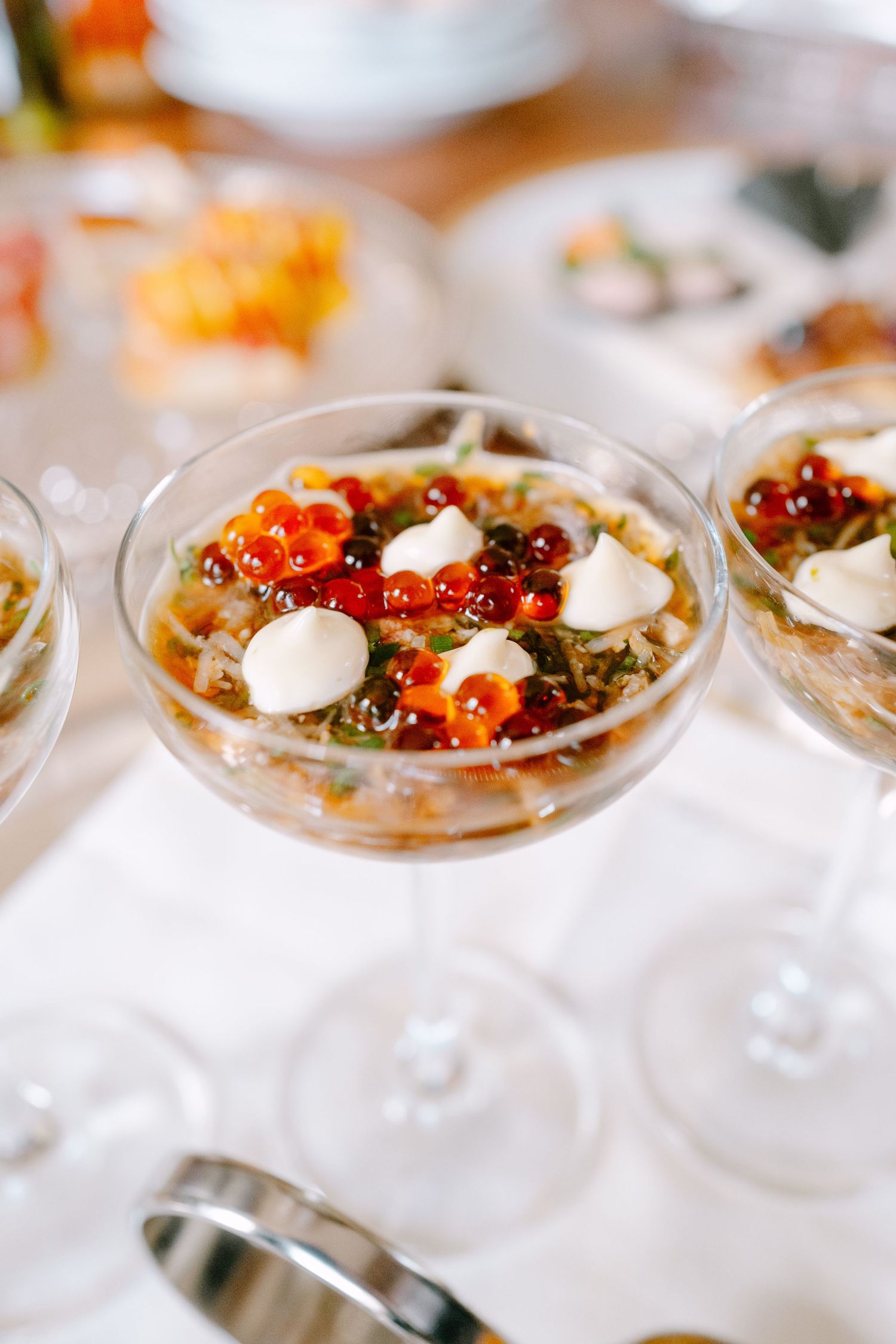 Elegant martini glasses filled with seafood appetizers topped with red caviar and cream dollops on a white tablecloth.
