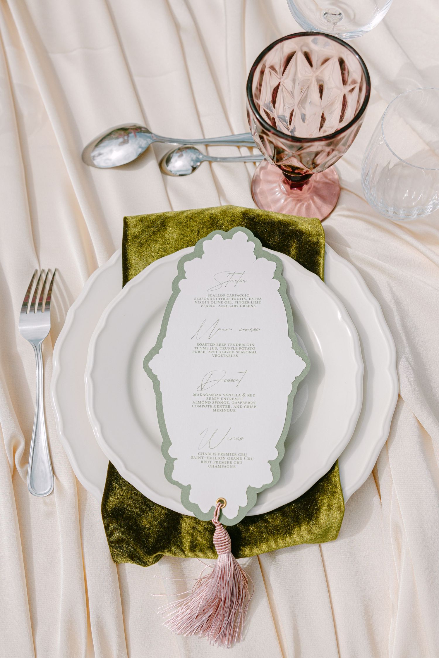 Elegant wedding place setting with green velvet napkin, ornate menu card, and pink glassware.