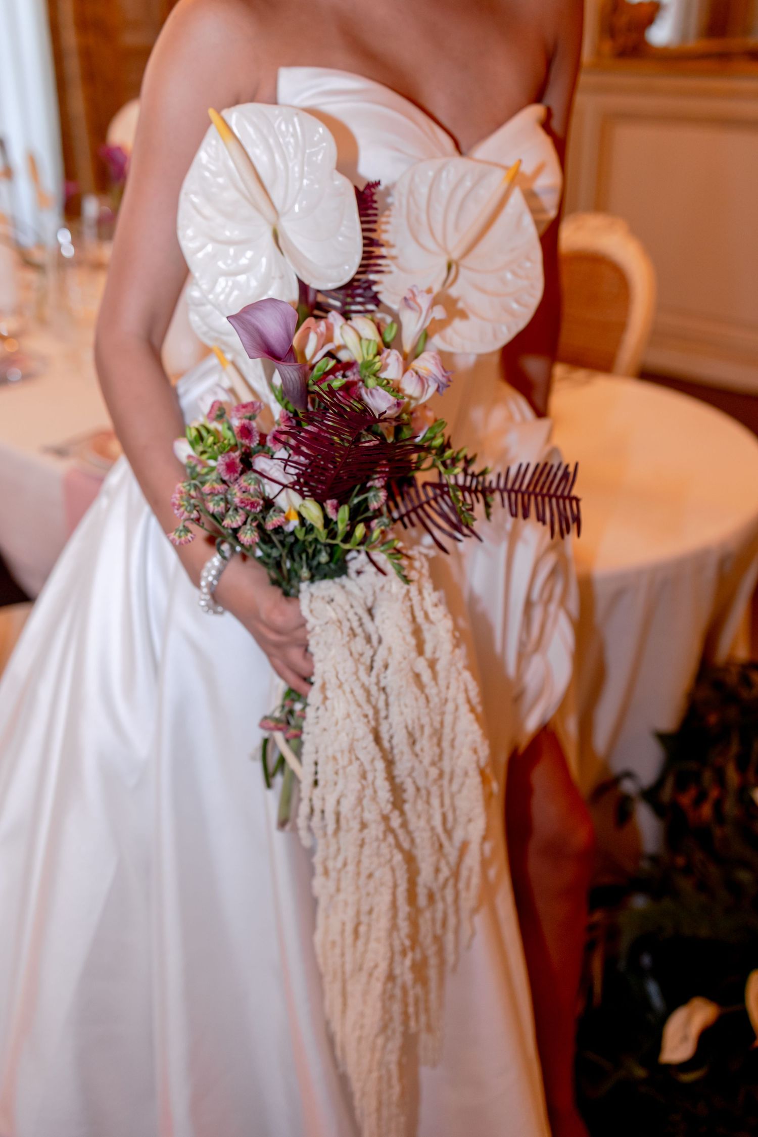 Bride in white strapless gown holding elegant bouquet with anthurium, calla lilies, burgundy ferns, and pampas grass.