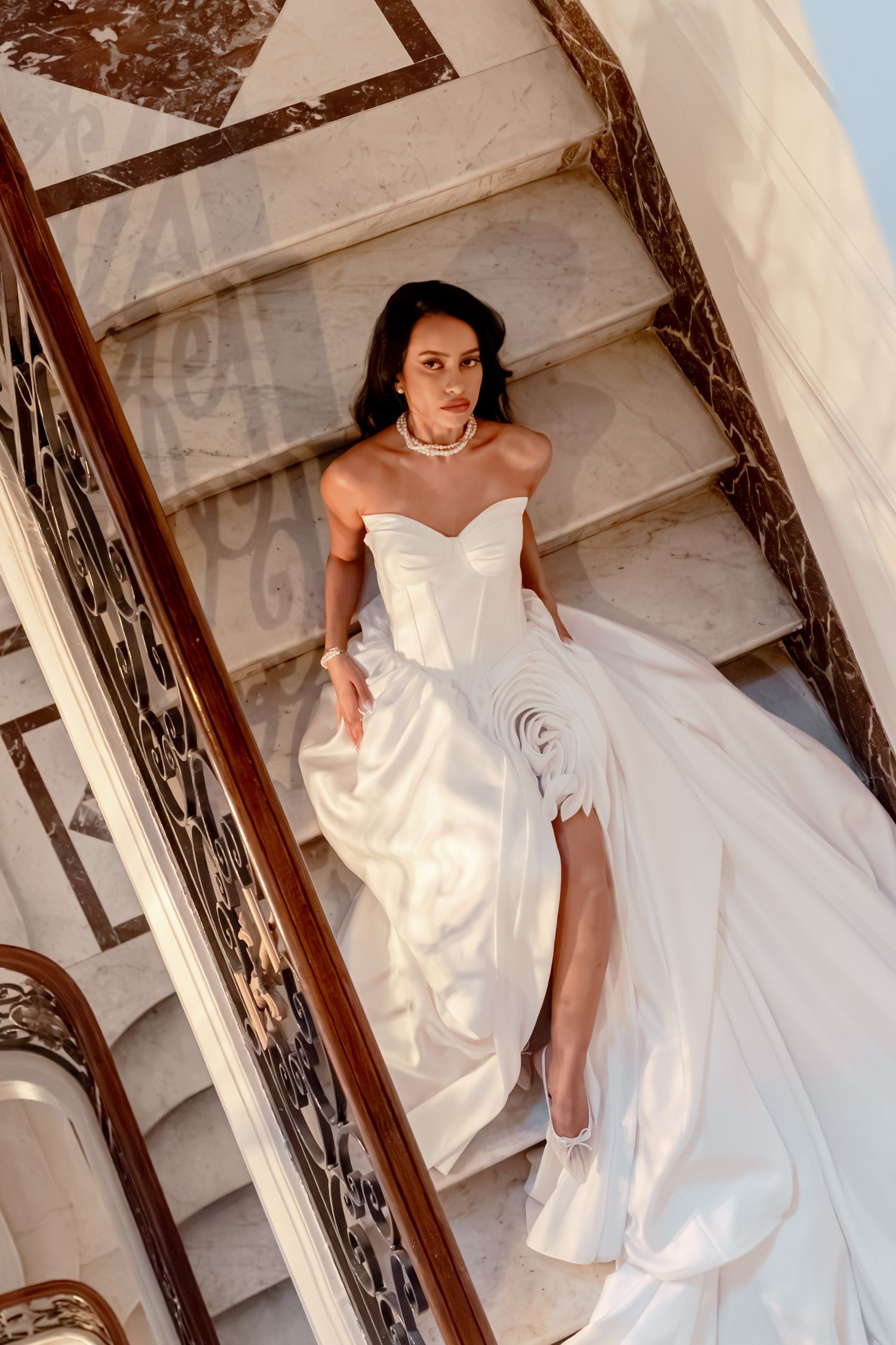 Stunning dark-haired bride in a strapless white ballgown lying gracefully on marble château staircase steps.