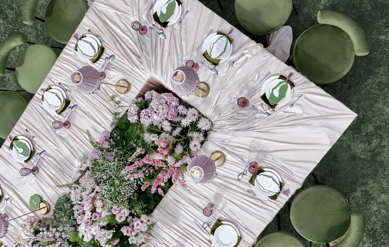 Aerial view of an elegant floral wedding table with pink blooms, green chairs, and white draped linen centerpiece.