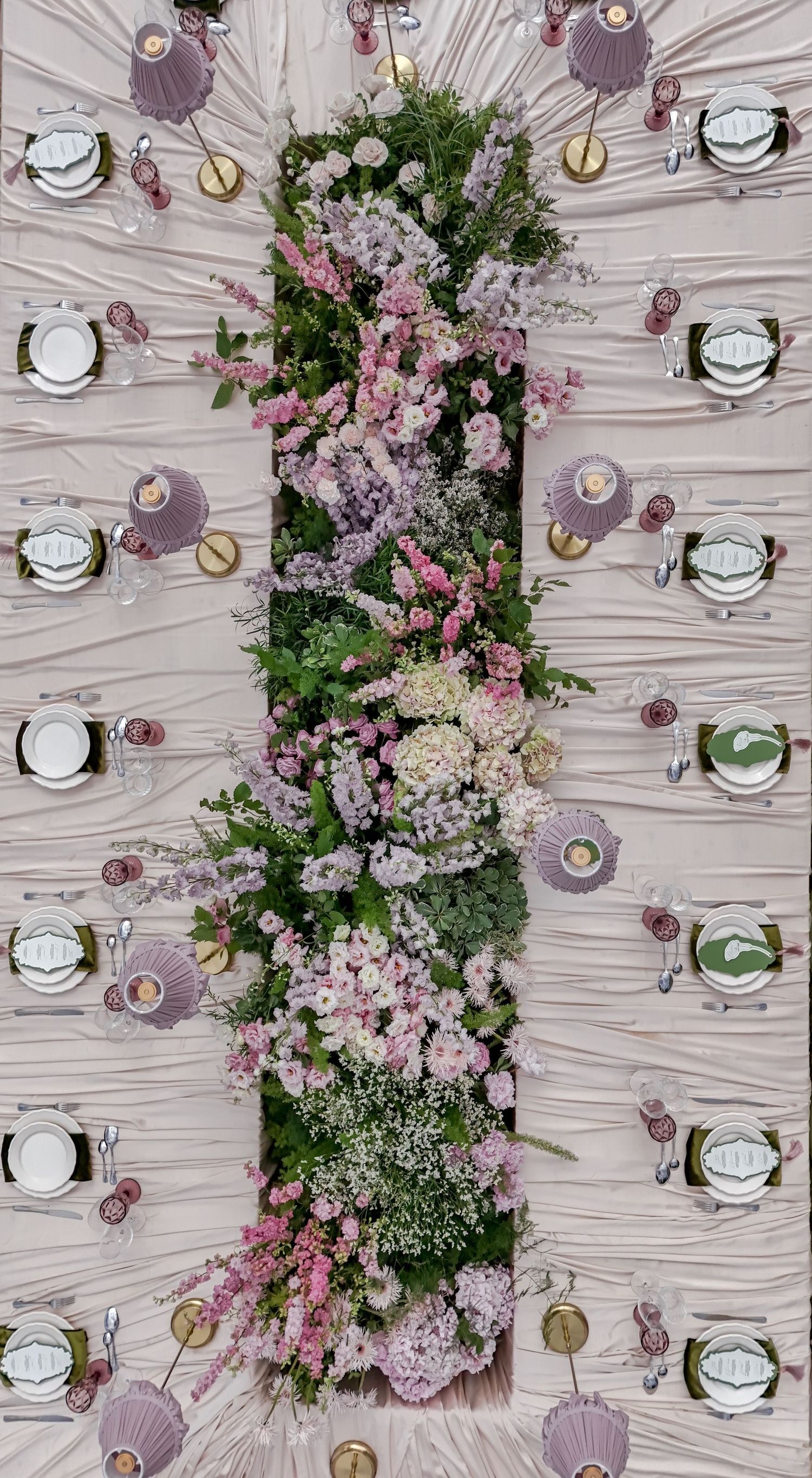 Aerial view of elegant wedding reception table with lush pink and lavender floral centerpiece and purple place settings.