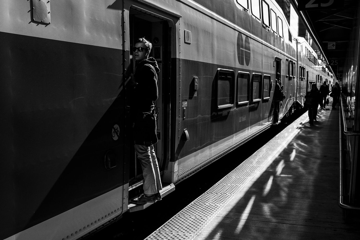 Black and white photo of a passenger boarding a double-decker train at a station platform.