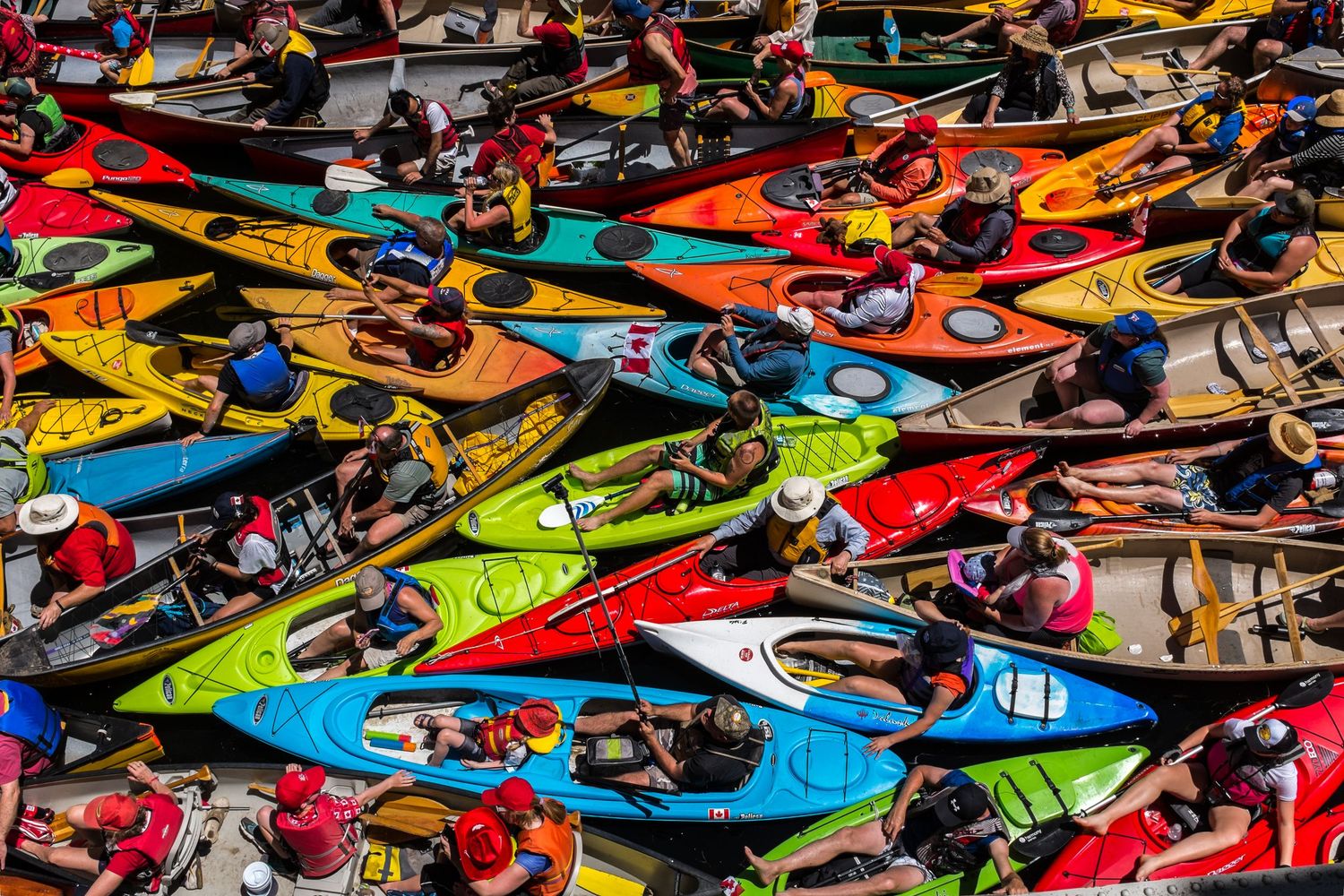 Aerial view of a vibrant crowd of colorful kayaks and paddlers packed together on the water.